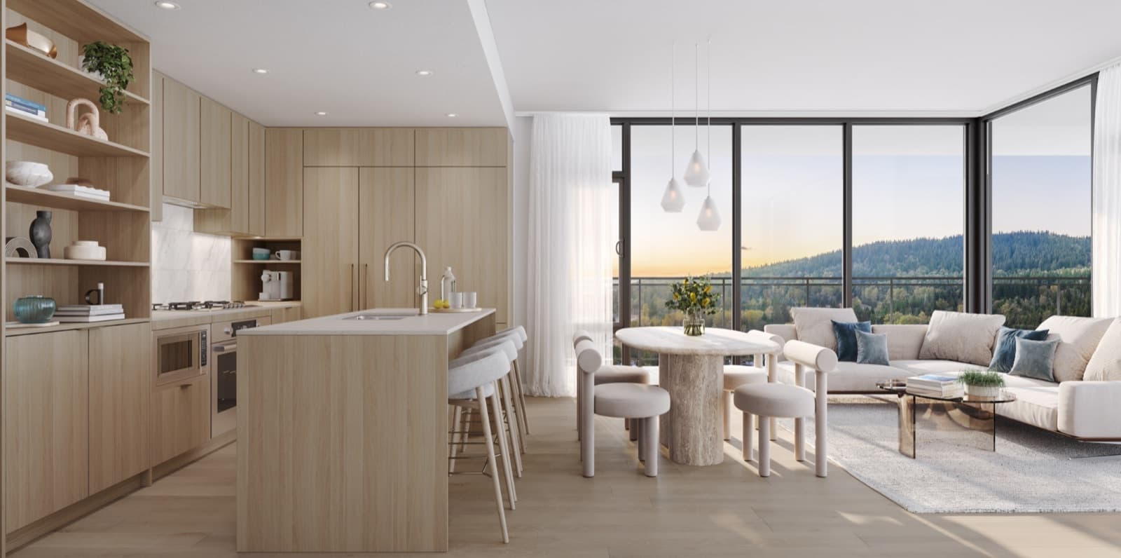 Komo – Open-concept kitchen, dining and living room in light wood tones with a round dining table, beige sectional sofa, and floor-to-ceiling windows showing a hillside sunset view.