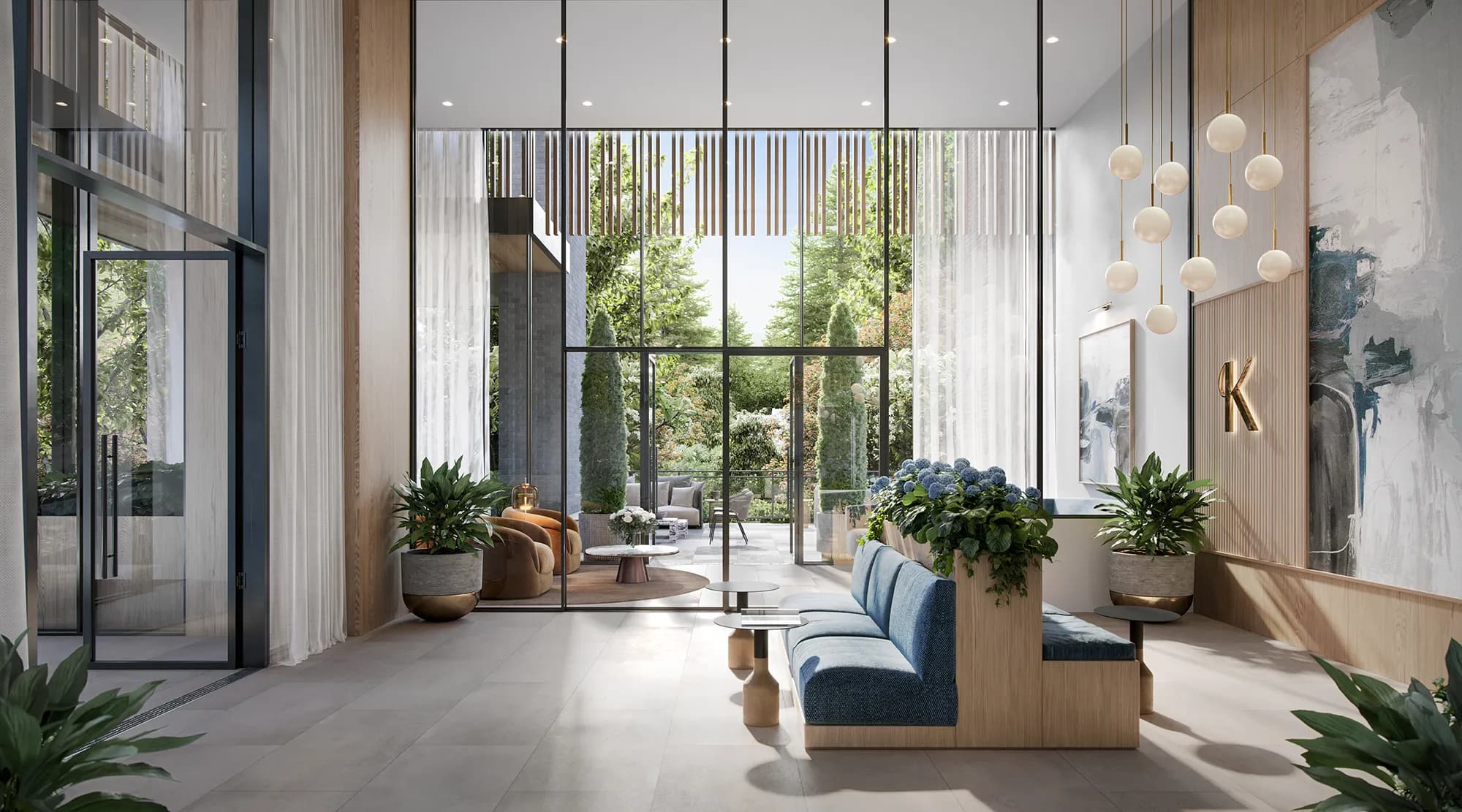 Komo – Double-height building lobby with floor-to-ceiling glass, a blue upholstered bench seat, pendant globe lighting, and a courtyard garden visible beyond.