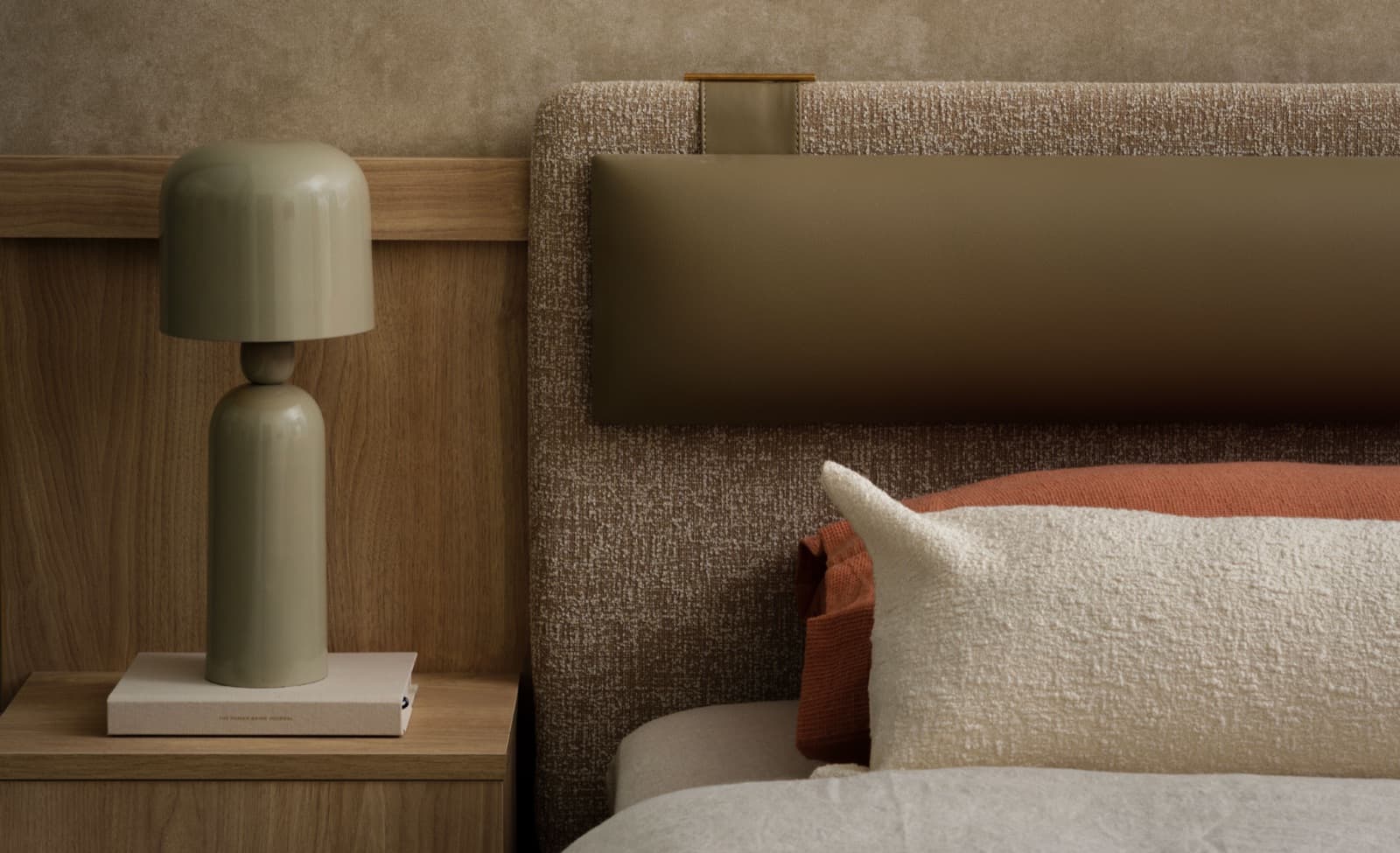 Komo – Close-up of a bedroom headboard detail with a ceramic table lamp, book, and layered cushions in warm neutral tones.