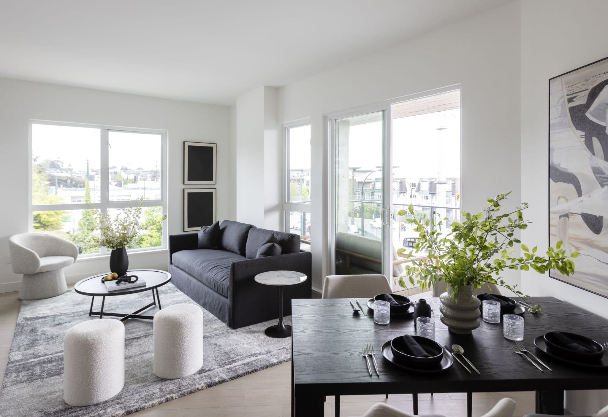 Innova – Living and dining room with a dark blue sofa, round coffee table, black dining table with place settings, and city-view windows.