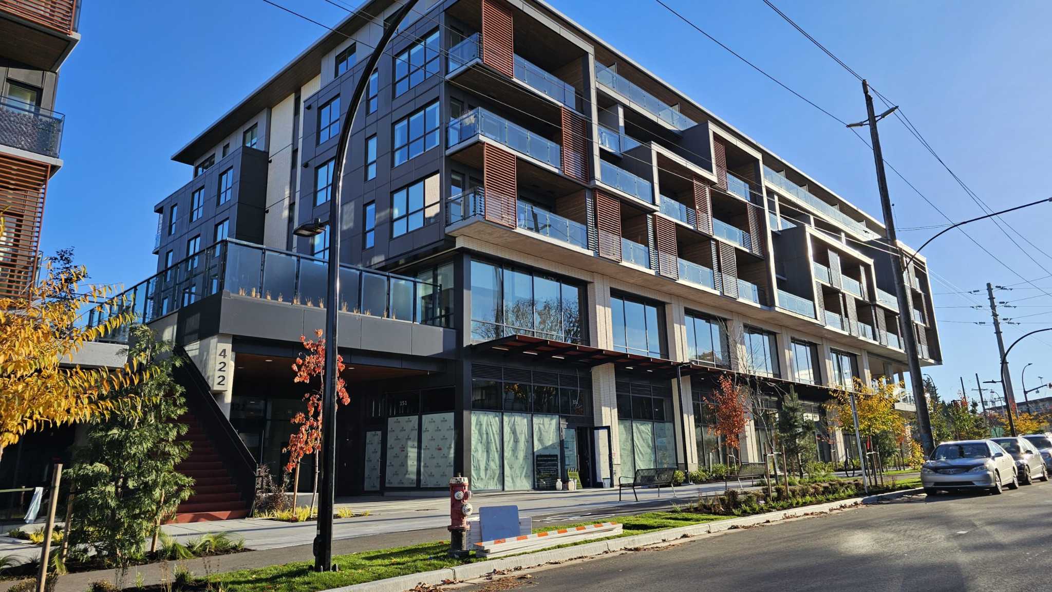Innova – Street-level daytime view of the modern multi-story building's dark facade with wood balcony screens and ground-floor retail units.