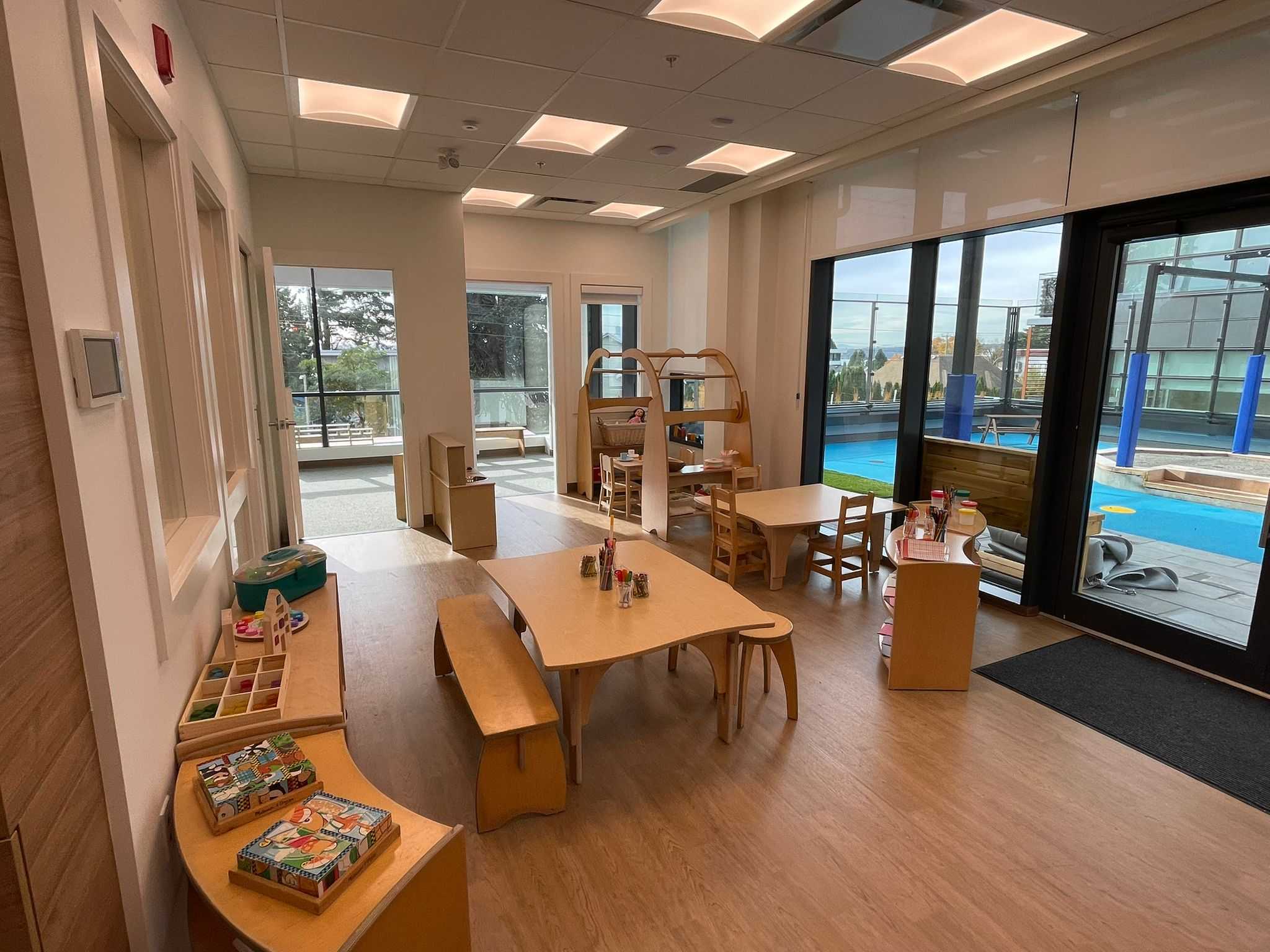 Innova – Children's playroom with small tables and chairs, toys, and glass doors opening onto an outdoor kids' pool and play area.