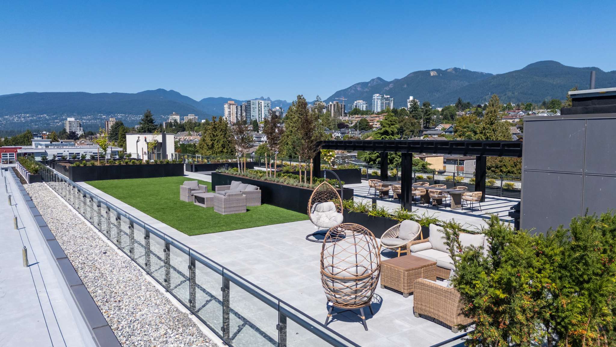 Innova – Rooftop terrace with artificial turf lawn, lounge seating, a pergola with dining tables, and mountain and city views.