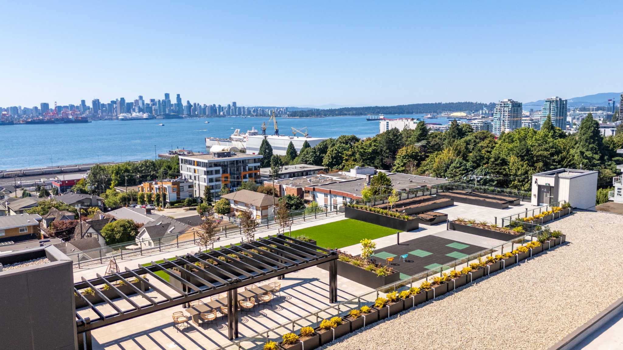 Innova – Rooftop terrace overlooking the water, city skyline, and mountains, with raised planter beds and outdoor seating.