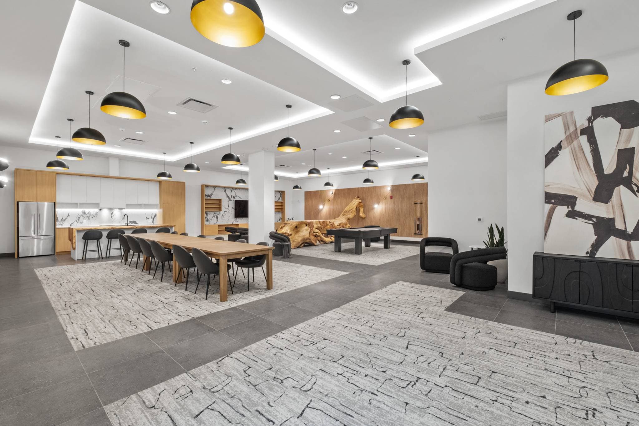 Innova – Shared lounge with a long dining table, kitchenette, driftwood sculpture, air hockey table, and large abstract artwork.