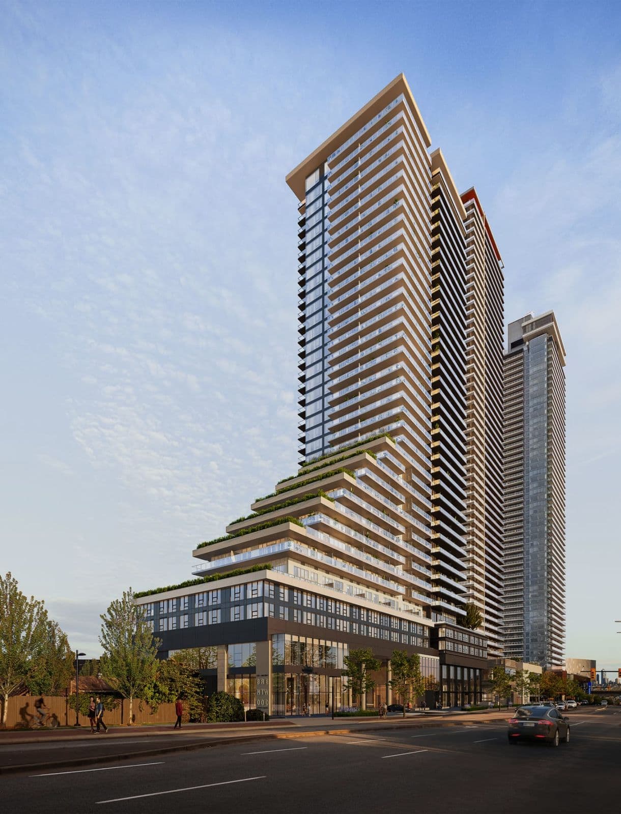 The Amazing Brentwood – Street-level view of the tapered high-rise tower with stepped green terraces near its base and a taller glass tower beside it, at dusk.