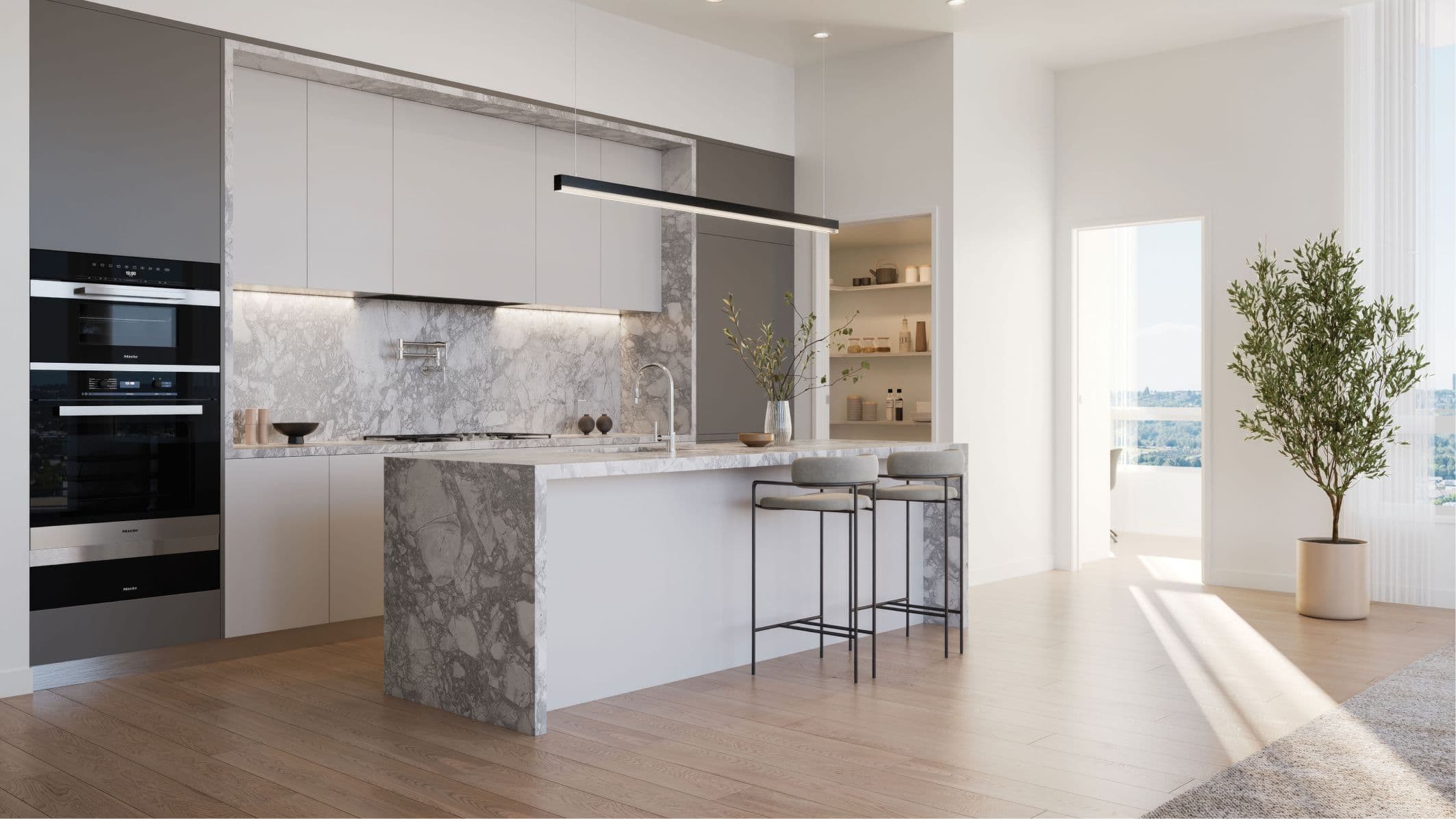 The Amazing Brentwood – Kitchen with light grey cabinetry, marble waterfall island with bar seating, built-in pantry nook, and a hallway leading to a bright room beyond.