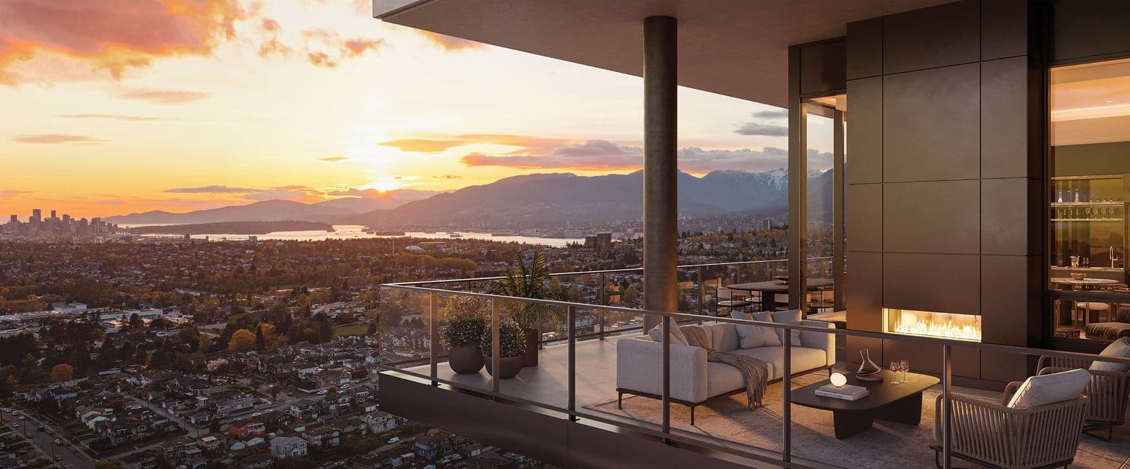 The Amazing Brentwood – High-rise balcony lounge area with sofa and fireplace overlooking a sunset skyline, mountains, and harbor in the distance.