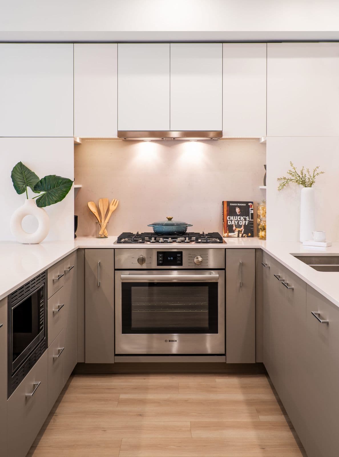1515 Rupert – Kitchen with white upper cabinets, gray lower cabinets, a stainless Bosch wall oven and gas cooktop, and a stone backsplash.