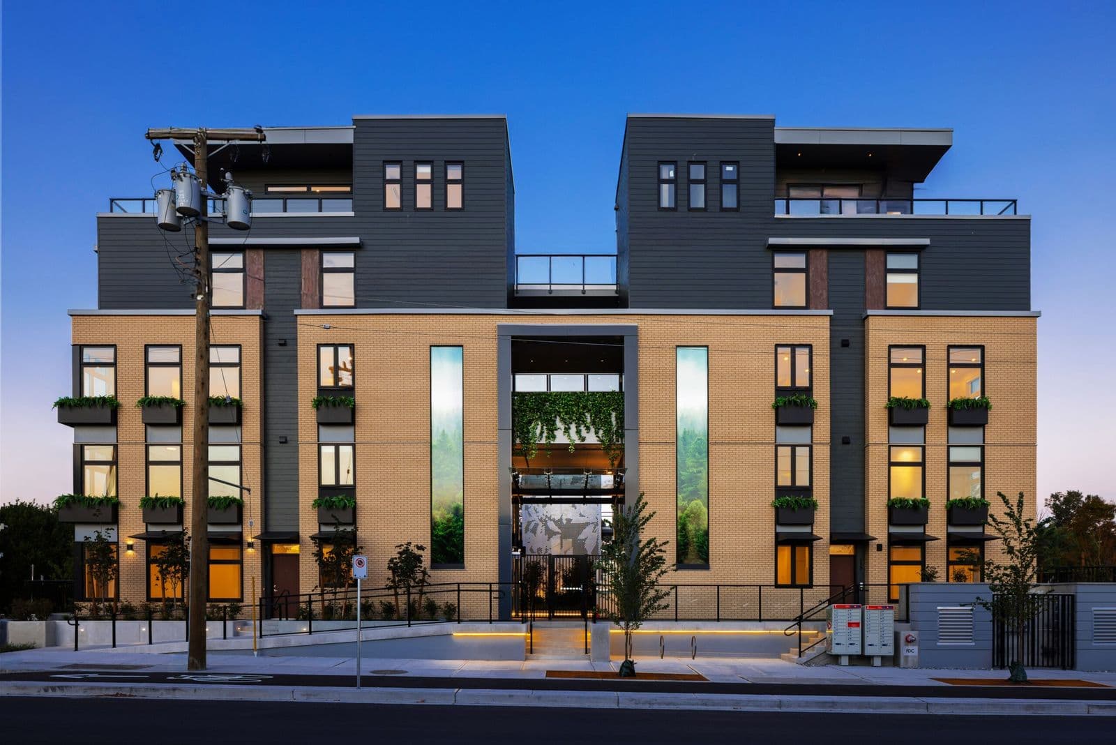 1515 Rupert – Dusk street-level view of the building's brick and dark-paneled facade with a lit entrance archway, window planter boxes and rooftop decks.