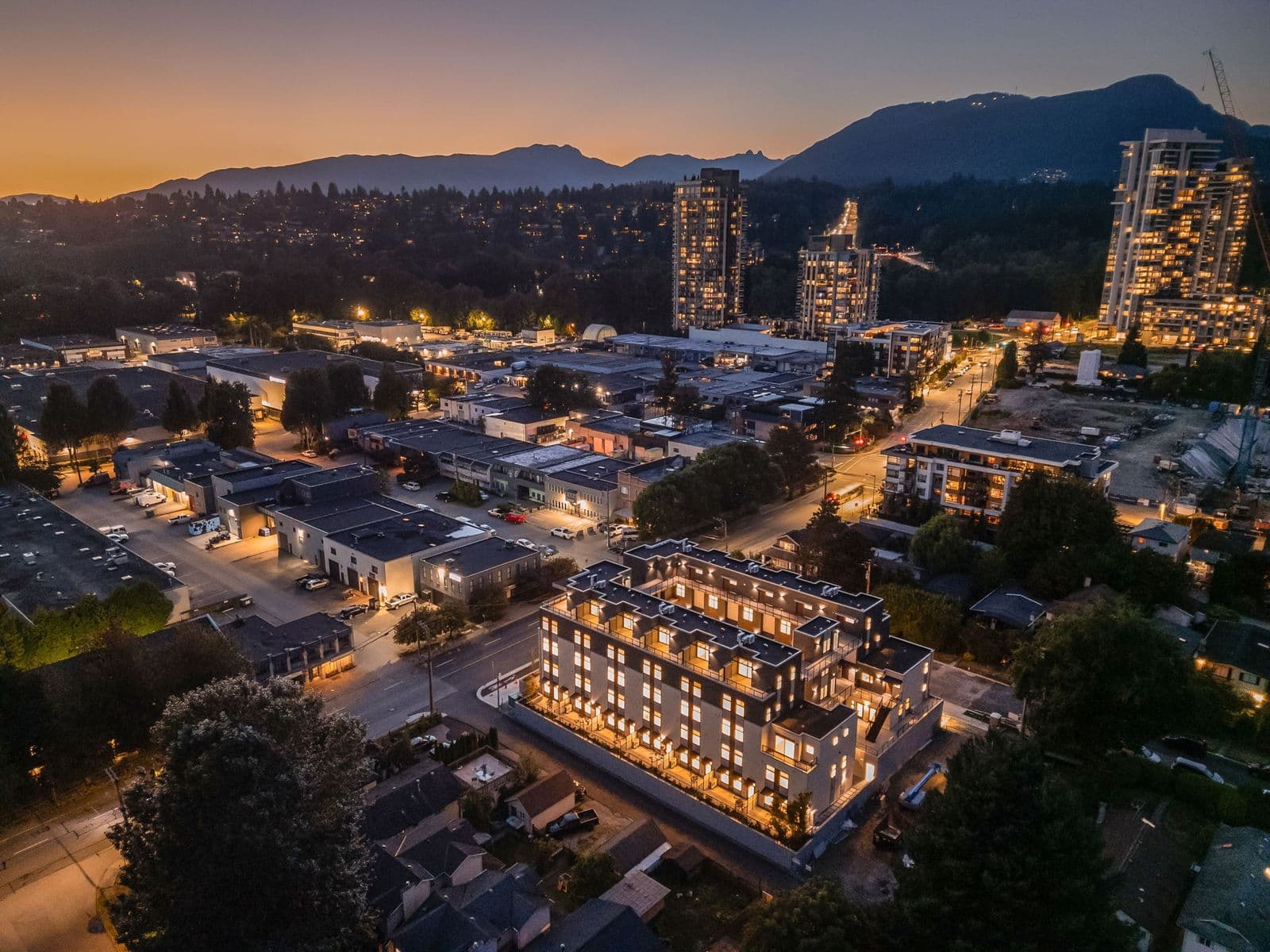 1515 Rupert – Twilight drone shot overlooking the lit-up building and surrounding neighborhood, with high-rise towers and mountains in the background.