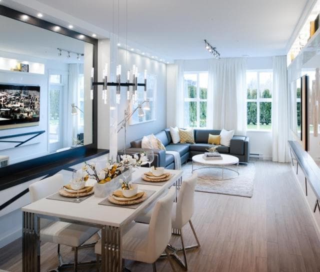 Union – Staged living and dining room with a blue sectional sofa, dining table set for four, and large mirror on the wall.