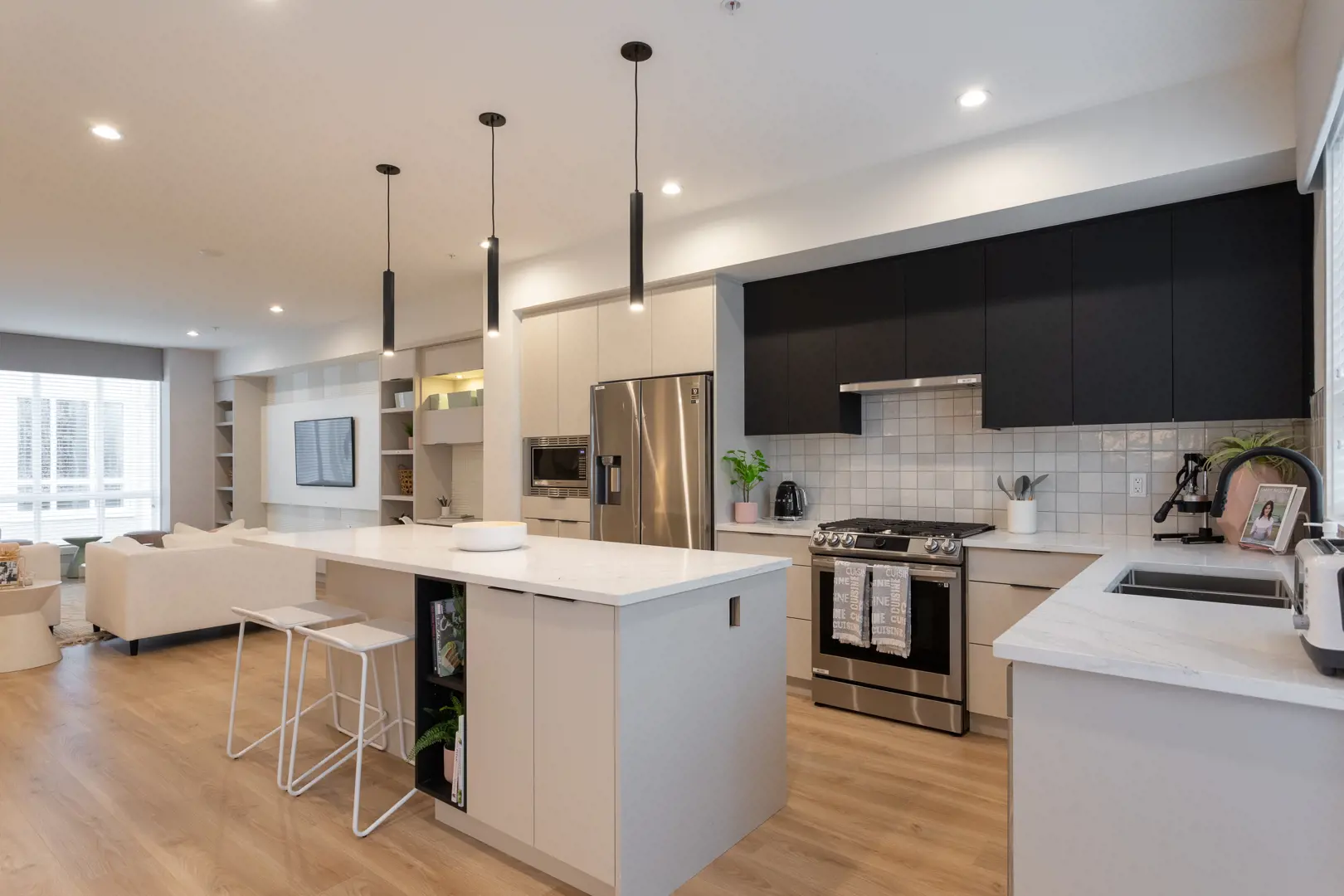 Union – Open-concept condo interior with kitchen island, black upper cabinets, stainless appliances, and living area with sofa.