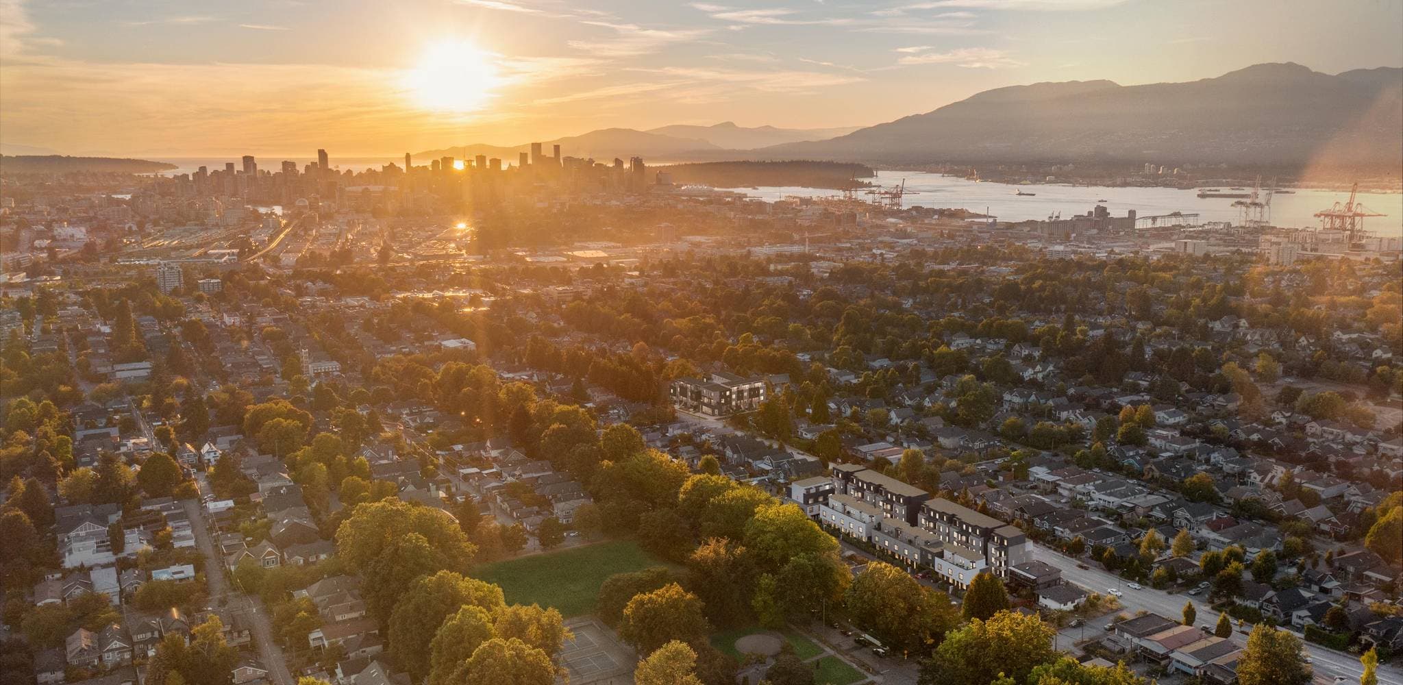 Templeton – Aerial sunset view of a low-rise development among residential streets with a downtown skyline and mountains in the distance.