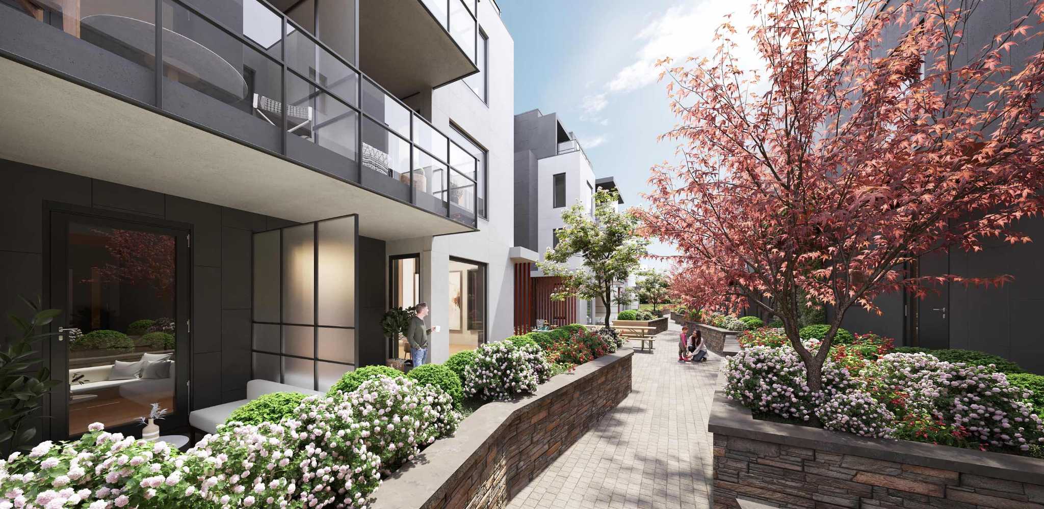 Templeton – A landscaped courtyard walkway between buildings with flowering shrubs, red maple trees, and a picnic table.