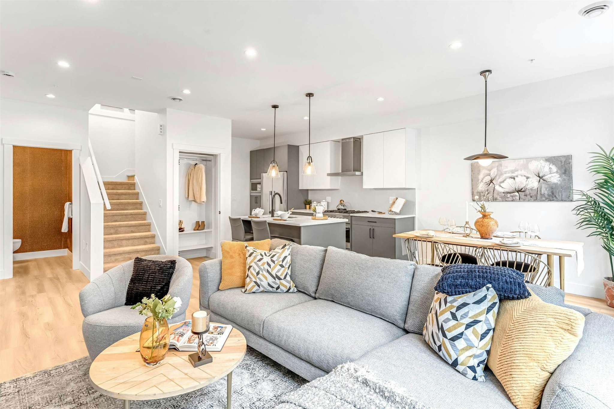 Park Avenue Townhomes – An open-concept living area showing a gray sectional sofa, adjacent dining table, and kitchen in the background.