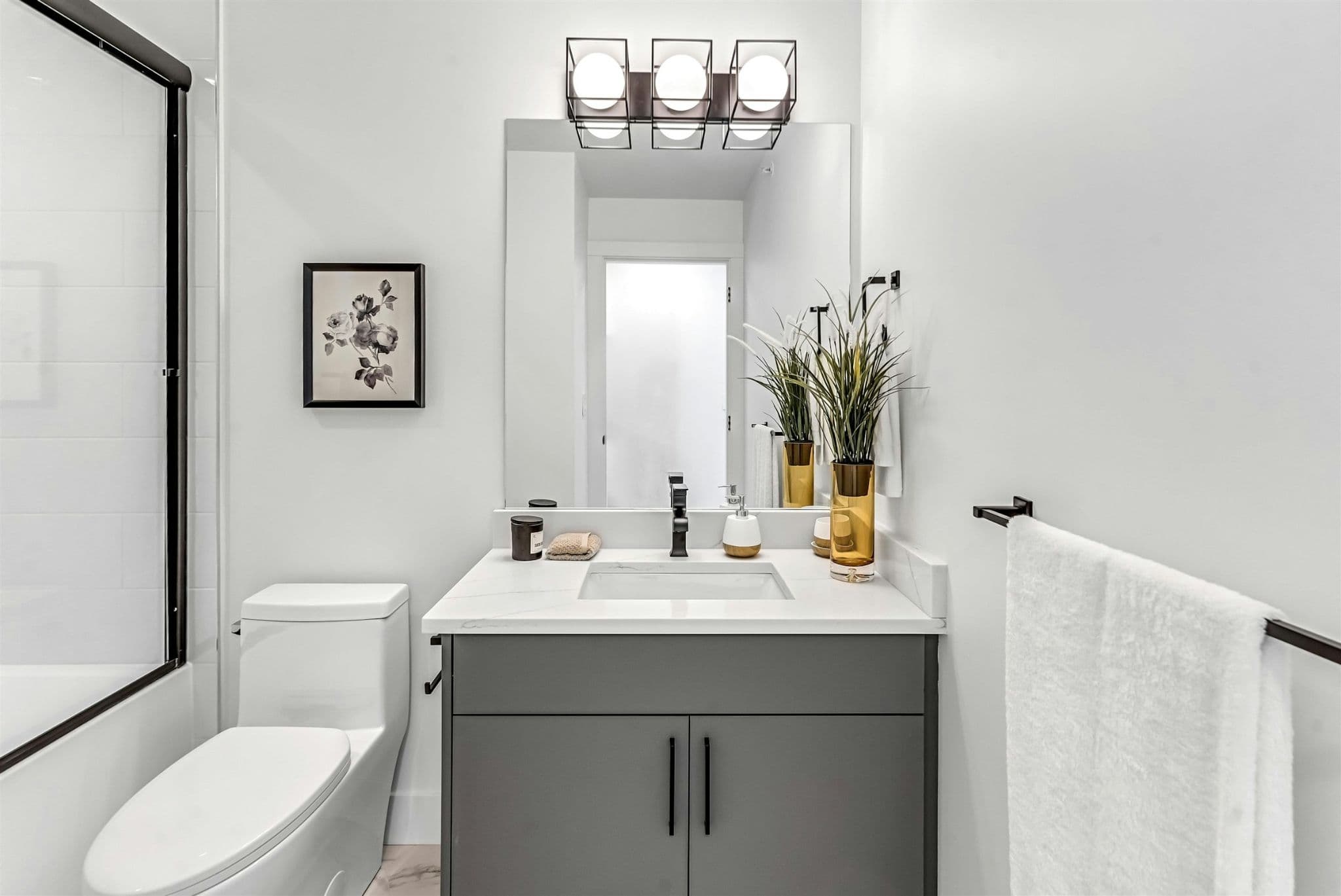 Park Avenue Townhomes – A contemporary bathroom featuring a vanity with gray cabinetry, a large mirror with modern vanity lighting, and a white toilet.