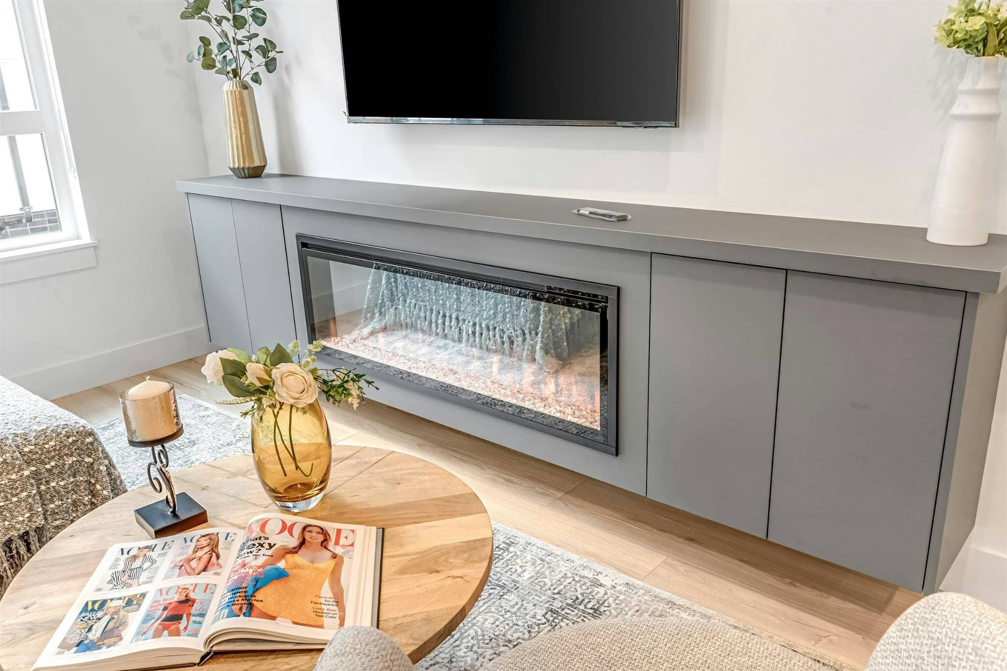 Park Avenue Townhomes – A cozy living space highlighting a built-in electric fireplace below a wall-mounted television and a round wooden coffee table.