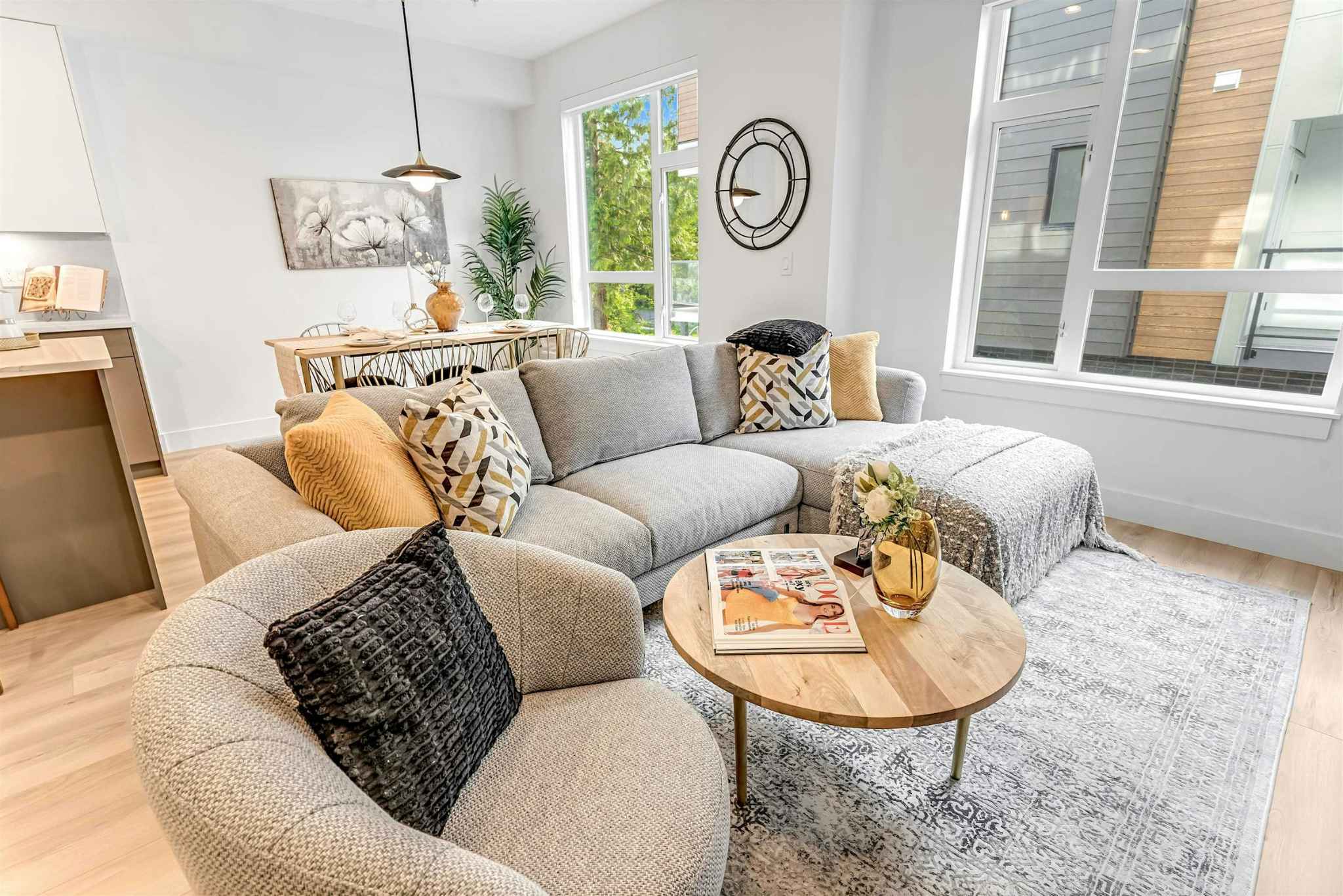 Park Avenue Townhomes – A bright living room with large windows, styled with a gray L-shaped sectional, round wooden table, and plush armchair.