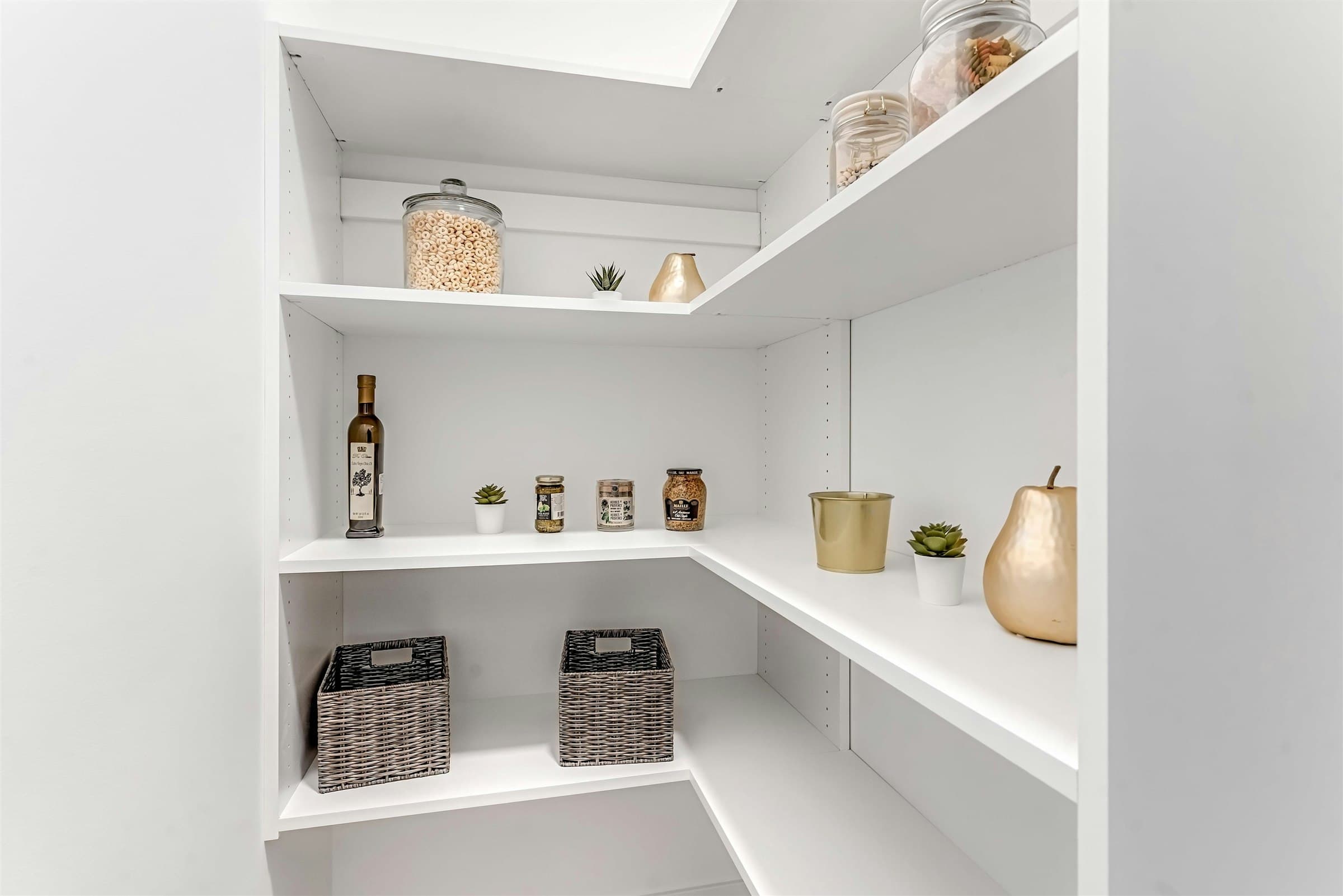 Park Avenue Townhomes – A walk-in kitchen pantry with custom white L-shaped shelving lined with glass jars, decorative items, and storage baskets.