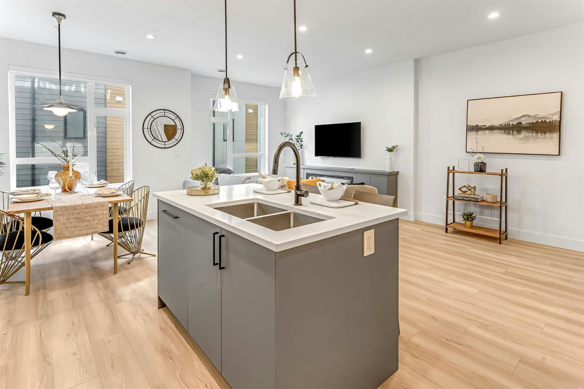 Park Avenue Townhomes – A broad view of the open kitchen island with pendant lights, open layout dining space, and adjacent living room with wood flooring.