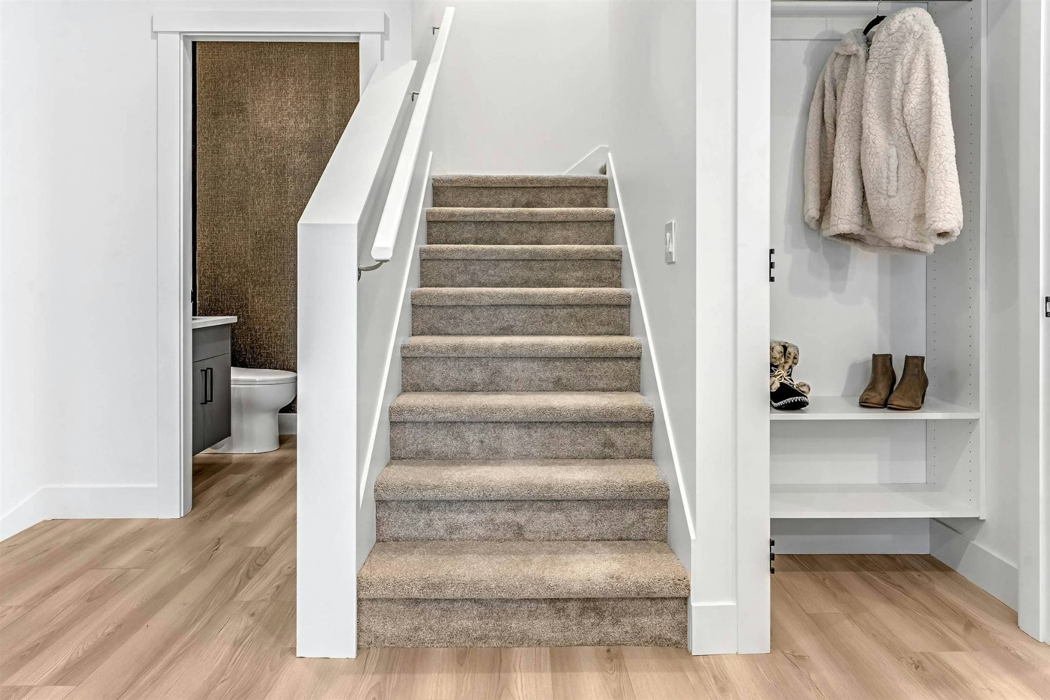 Park Avenue Townhomes – A carpeted staircase leading to the upper level, positioned between a powder room doorway and an entryway closet.