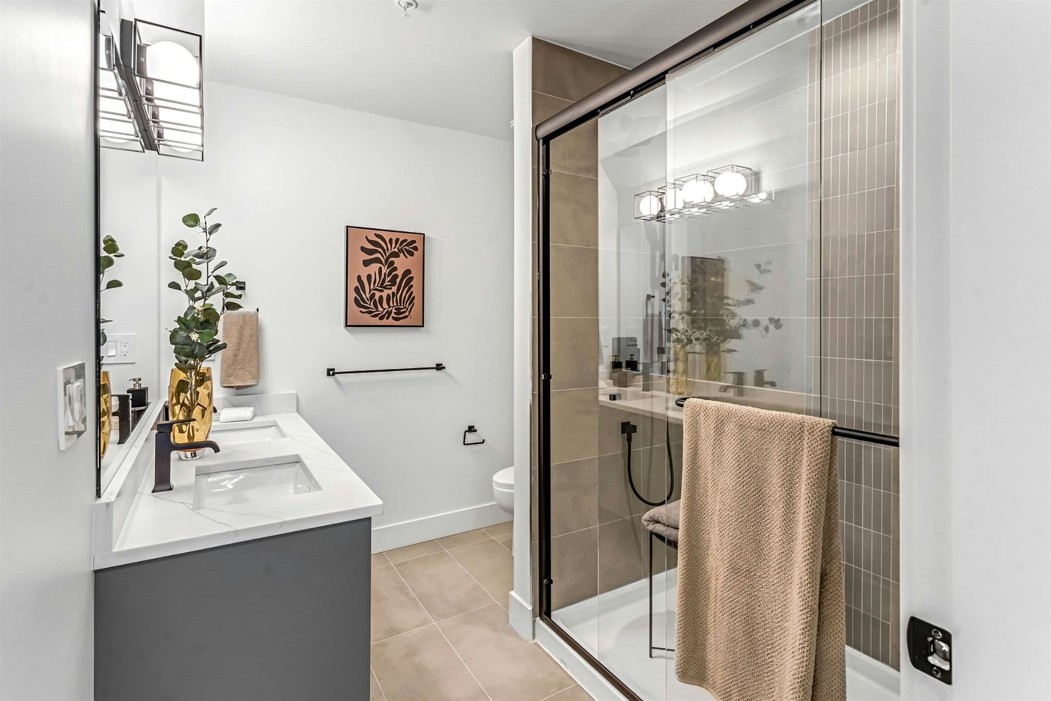 Park Avenue Townhomes – An ensuite bathroom with double vanity sinks, dark gray cabinetry, and a glass-enclosed walk-in shower with tile accents.