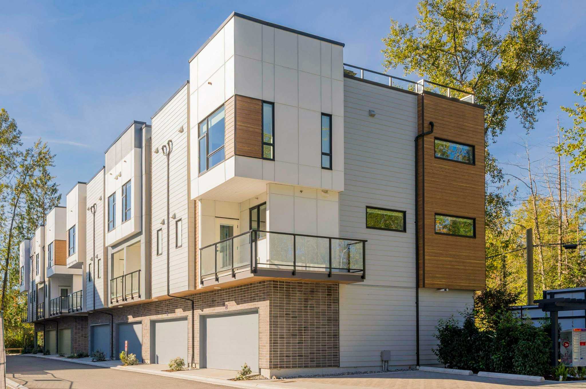 Park Avenue Townhomes – Exterior view of modern multi-level townhomes featuring light siding, wood-toned accents, glass balcony railings, and ground-floor garages.