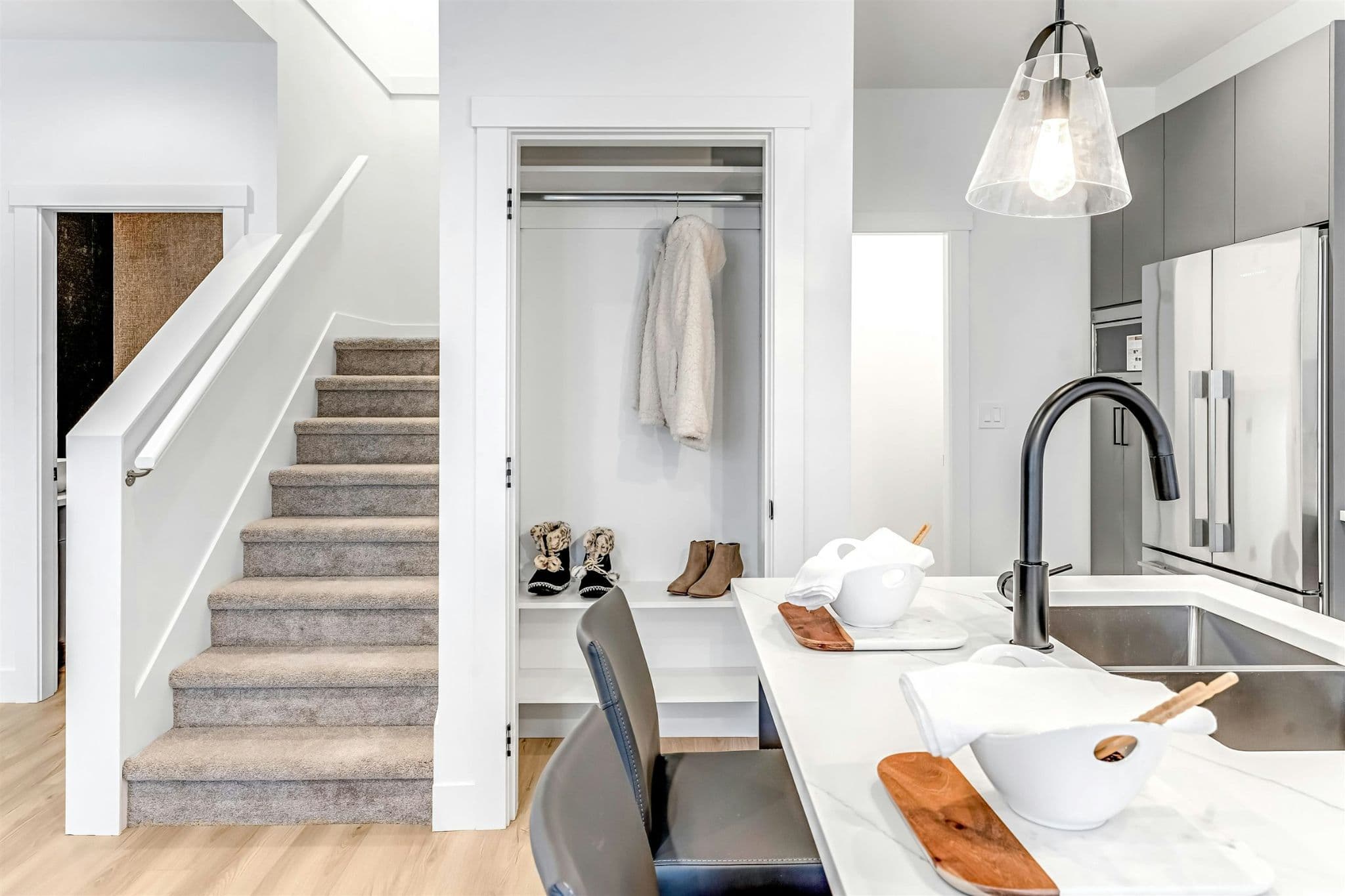 Park Avenue Townhomes – An interior foyer and kitchen area featuring carpeted stairs, a coat storage niche, and the edge of a kitchen island bar.
