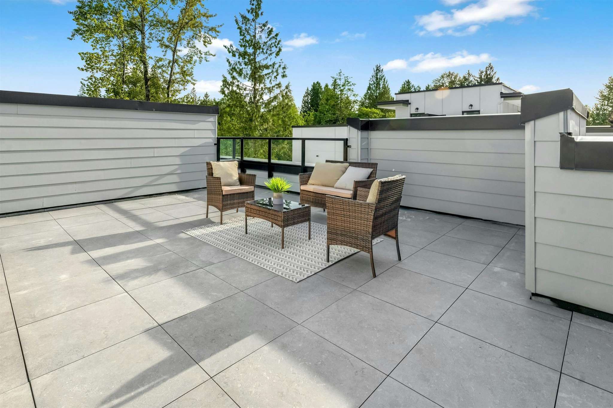 Park Avenue Townhomes – A spacious rooftop patio furnished with a wicker patio seating set, coffee table, outdoor rug, and glass railing.