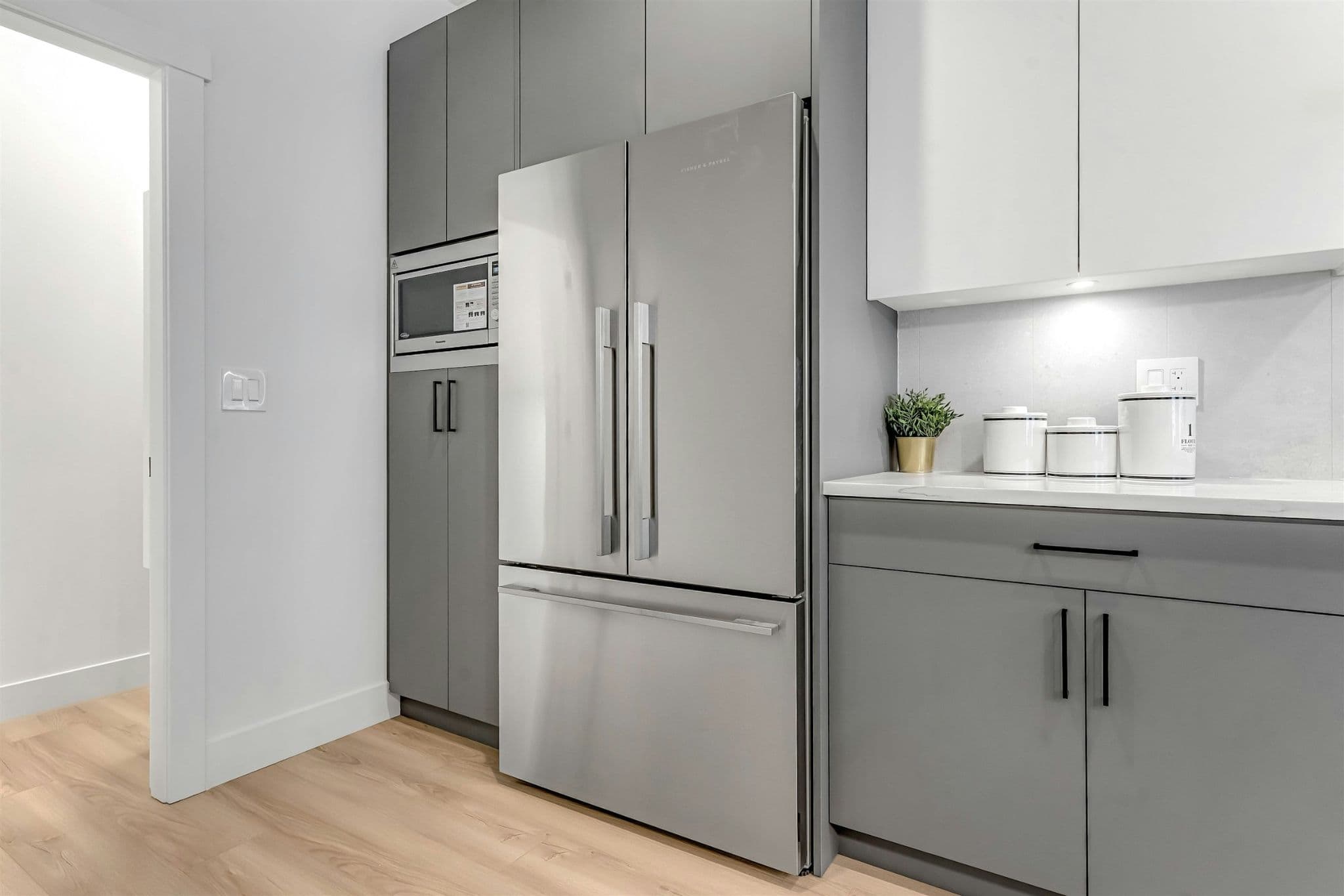 Park Avenue Townhomes – A kitchen detail showing a stainless steel French door refrigerator, built-in microwave, grey cabinetry, and white upper cabinets.