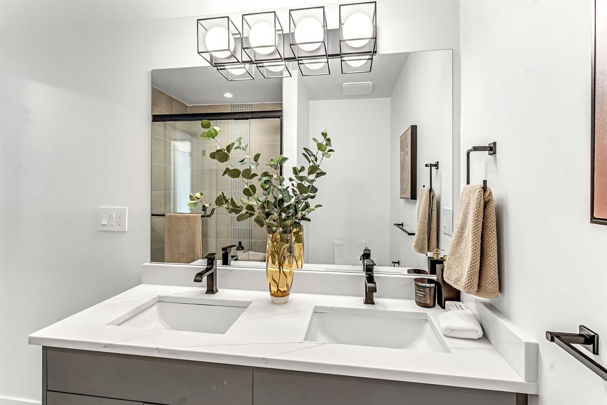 Park Avenue Townhomes – A double-sink bathroom vanity with white quartz countertop, black fixtures, rectangular mirror, and modern lighting fixture.