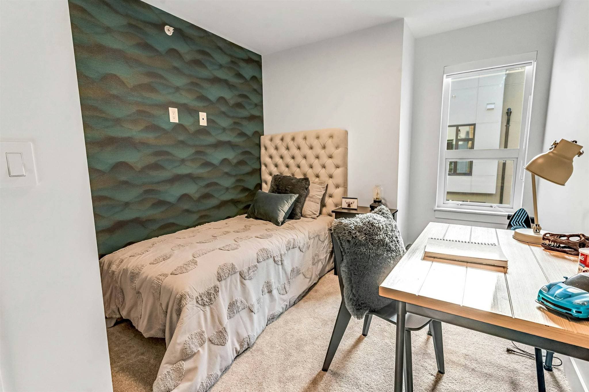 Park Avenue Townhomes – A cozy bedroom setup featuring a tufted headboard bed against a teal textured accent wall, alongside a desk workspace.