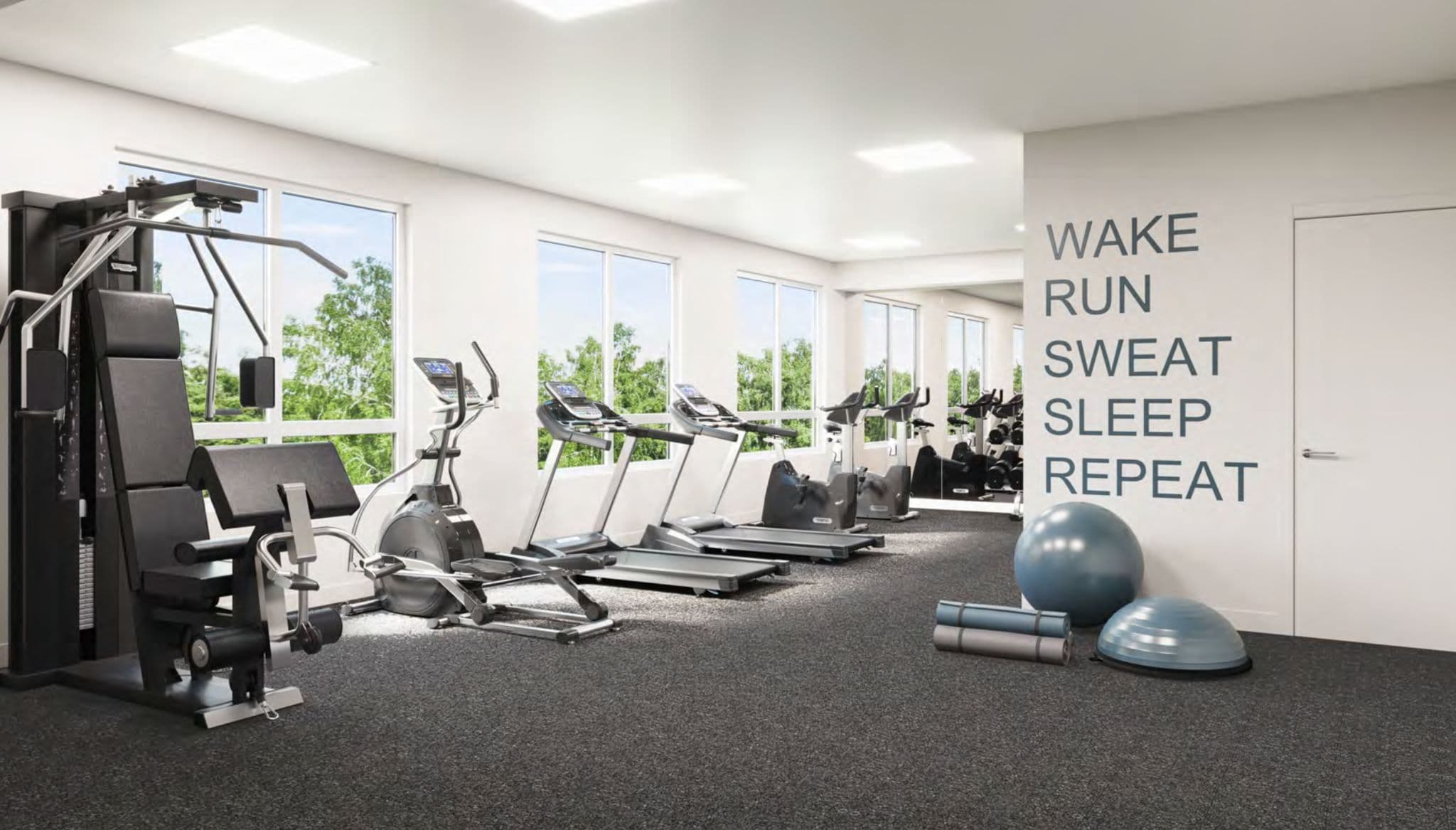 JEM Condos – Fitness room with treadmills, an elliptical, a weight machine, exercise balls, and floor-to-ceiling windows overlooking trees.