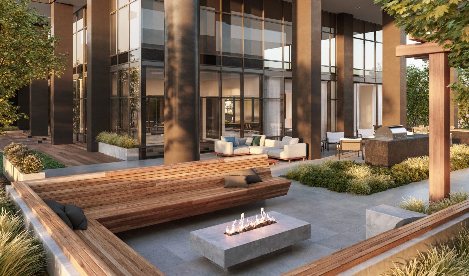 Jinju – A luxurious outdoor amenity terrace featuring a sunken wooden bench surrounding a modern linear fire pit, bathed in warm golden-hour sunlight. In the background, landscaped greenery and lounge seating flank an outdoor kitchen with a built-in BBQ grill beneath a modern glass and steel residential tower.