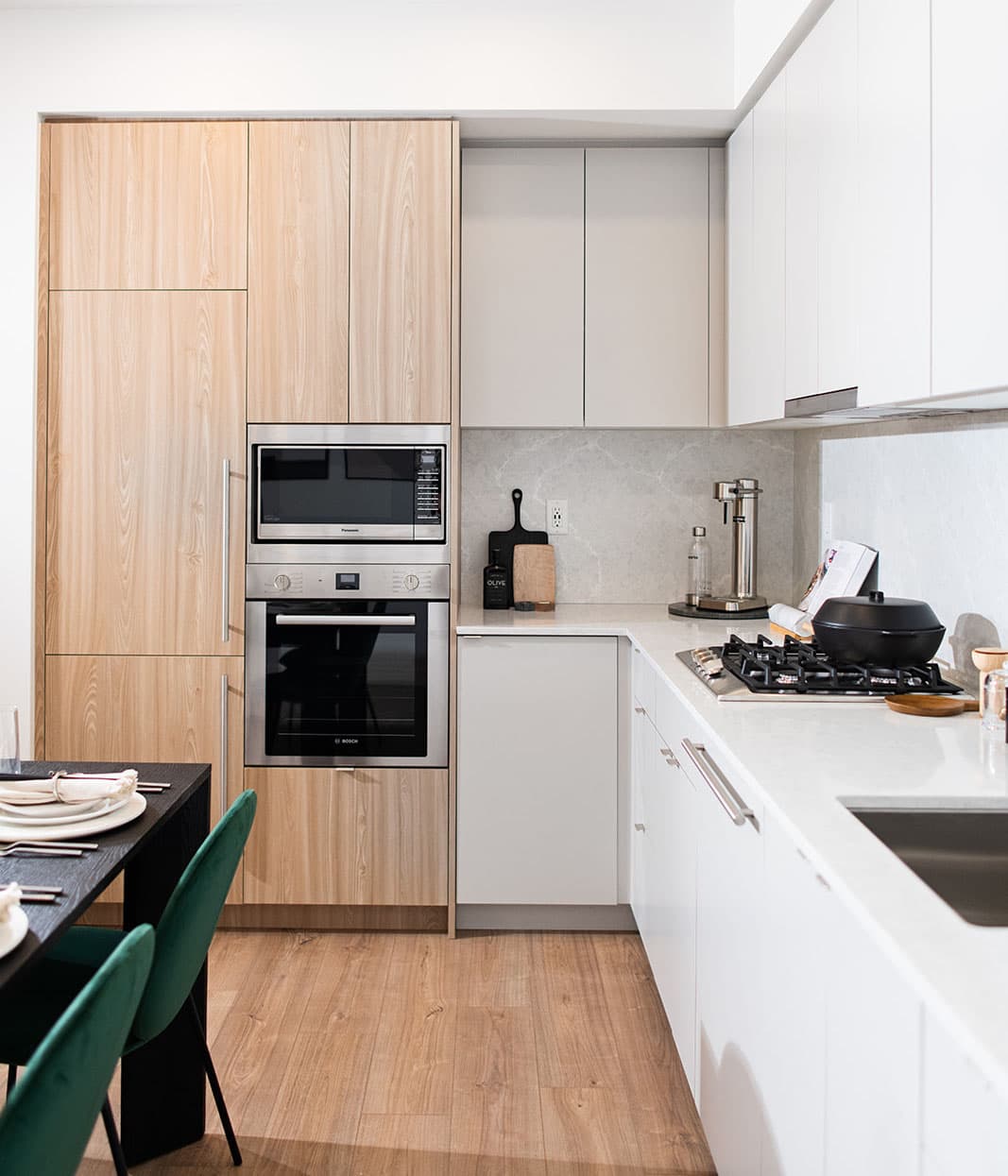 Jinju – A modern kitchen with light wood cabinets, built-in microwave and oven, gas cooktop, and a dining table with green chairs.