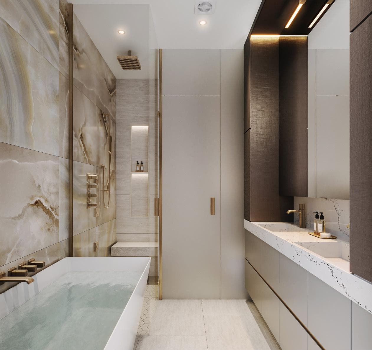 Italia – A luxury bathroom with book-matched marble-look feature wall, a freestanding soaking tub filled with water, brass fixtures, a glass shower with bench, and a double vanity.