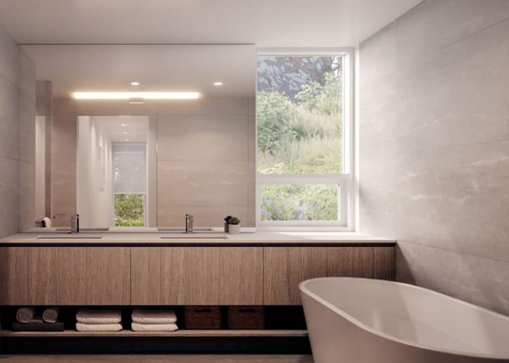 Alpine – Bathroom with a double vanity, wood cabinetry, and a window overlooking greenery, plus a freestanding tub.