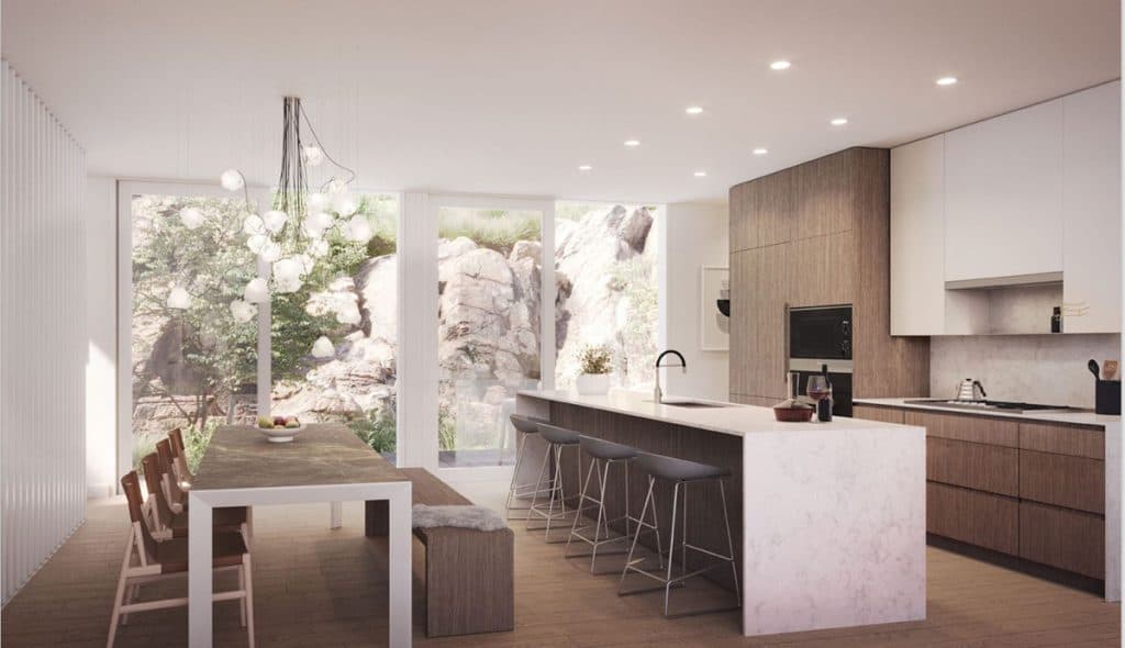 Alpine – Kitchen and dining area with a wood dining table, bar stools at a marble island, and a large window looking onto a rocky garden.