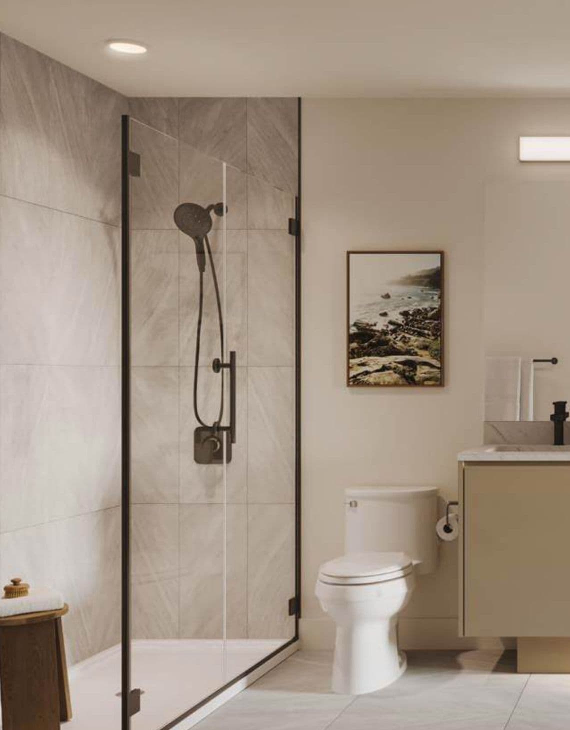 Eden – Bathroom with a glass-enclosed shower and handheld showerhead, marble tile walls, a white toilet, and a beige vanity with framed coastal artwork.