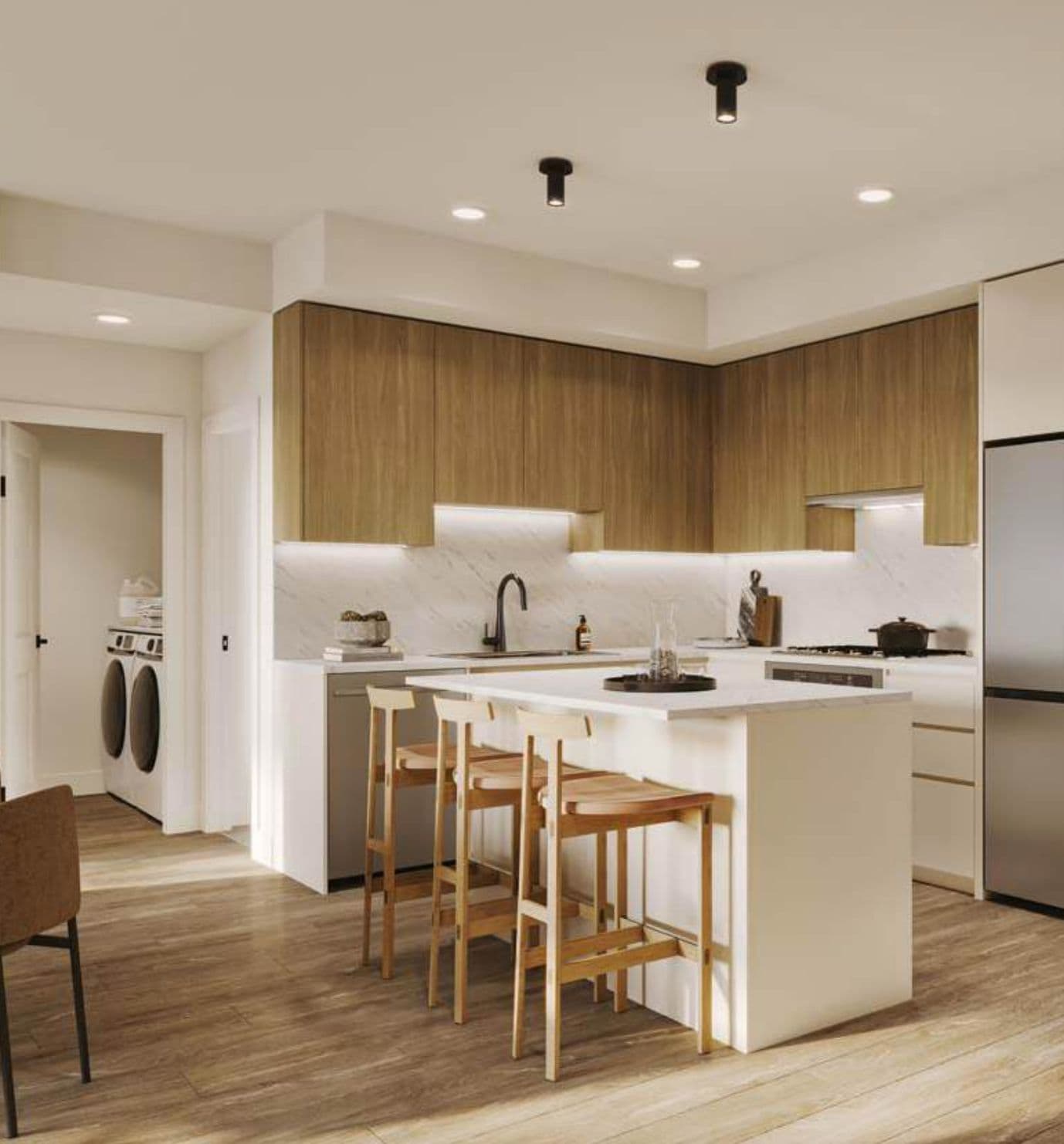 Eden – Kitchen with wood-grain upper cabinets, marble backsplash, an island with wood bar stools, stainless fridge, and a laundry nook off to the side.