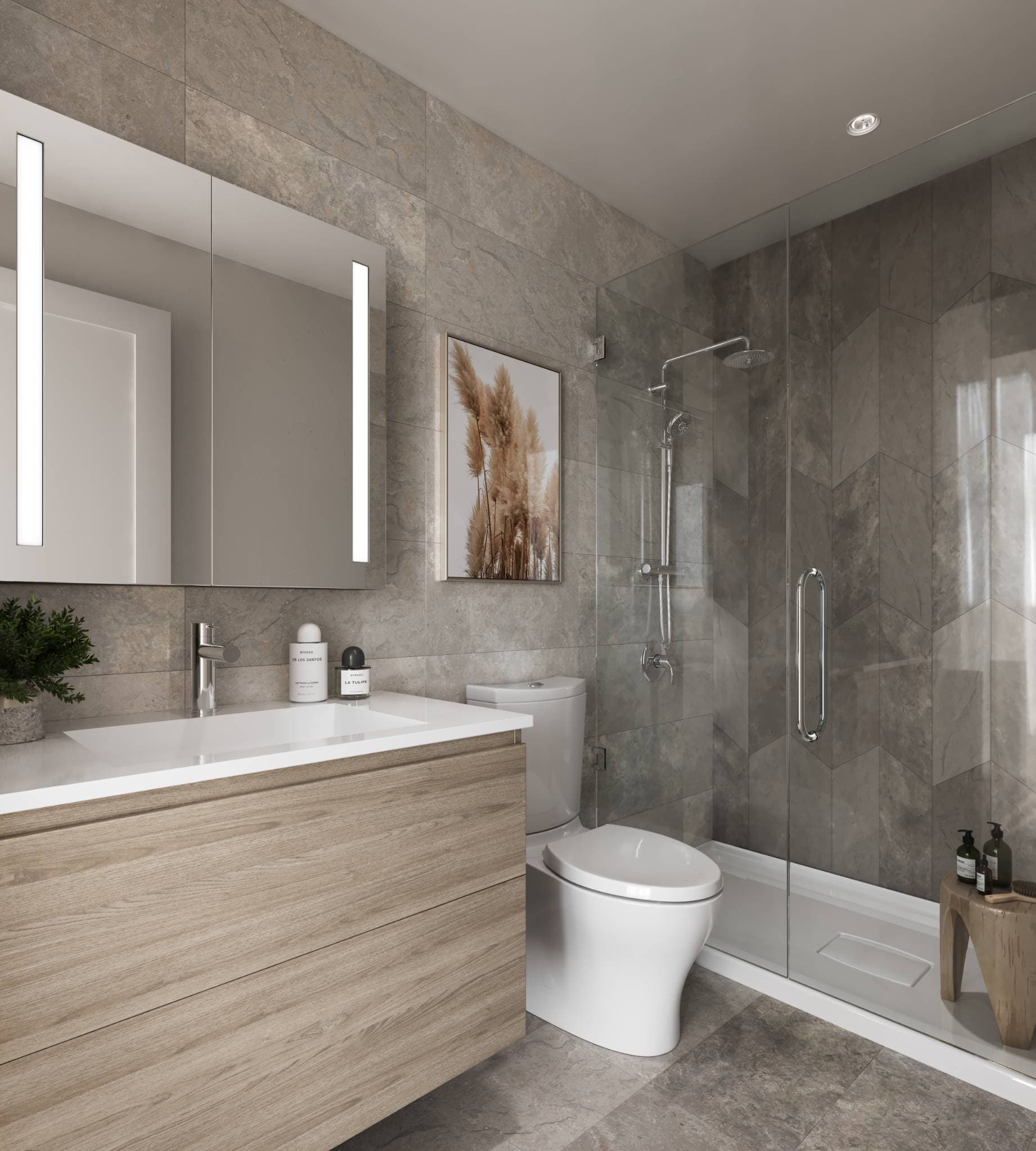 Sequoia – A modern bathroom featuring a floating light-wood vanity, an illuminated medicine cabinet mirror, and a glass-enclosed walk-in shower with chevron-patterned grey tile. The walls and floors are clad in large grey stone tiles, creating a sleek, contemporary atmosphere.
