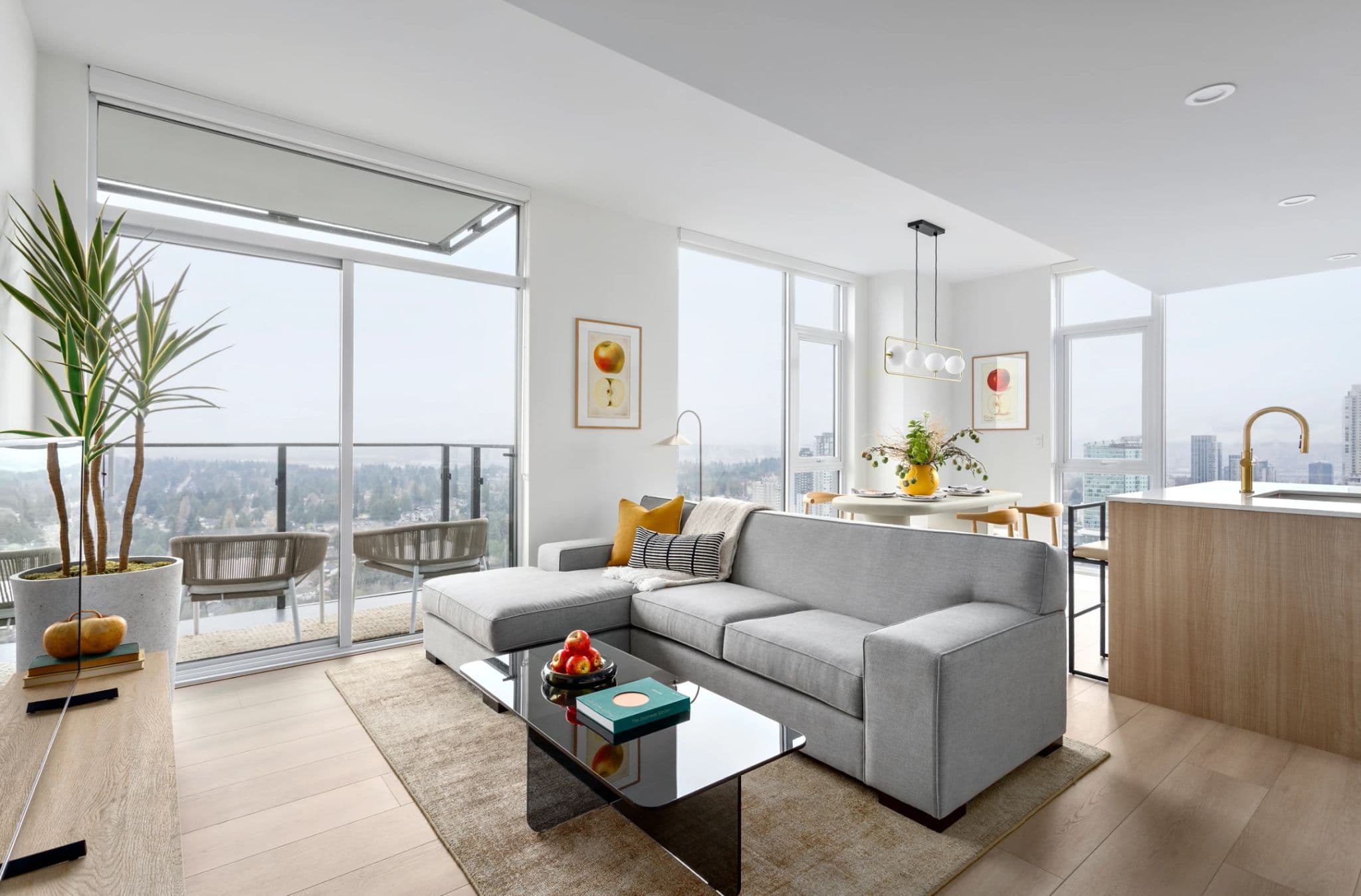 Century City Holland Park - Park Tower 1 – Living room with a grey sectional sofa, glass coffee table, and floor-to-ceiling windows leading to a balcony with outdoor seating and a hazy view.