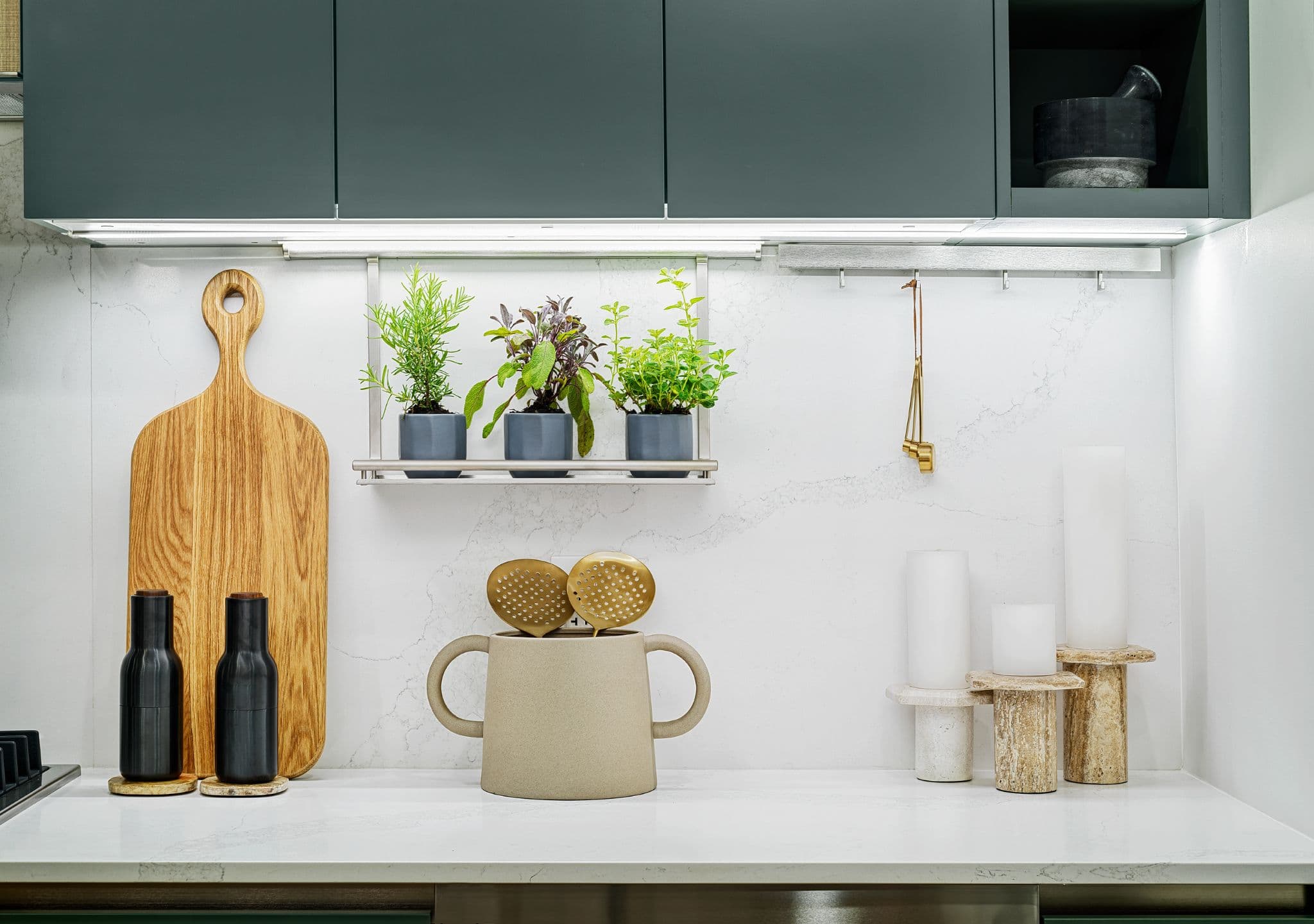 Century City Holland Park - Park Tower 1 – Kitchen countertop styling detail with a wood cutting board, potted herbs on a rail, and decorative candle holders against a marble backsplash.