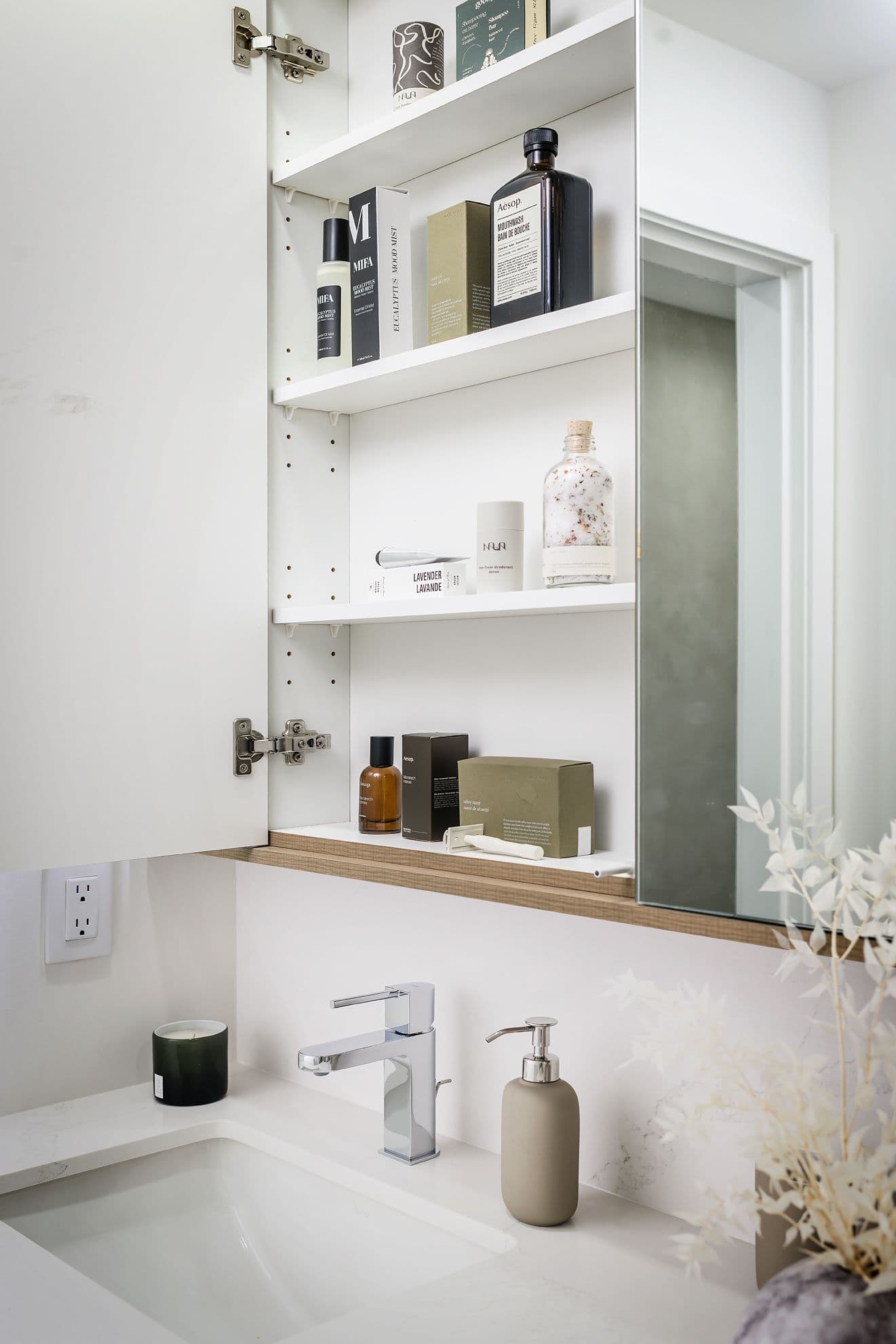Century City Holland Park - Park Tower 1 – Close-up of an open bathroom medicine cabinet stocked with skincare and grooming products above a sink with chrome faucet.