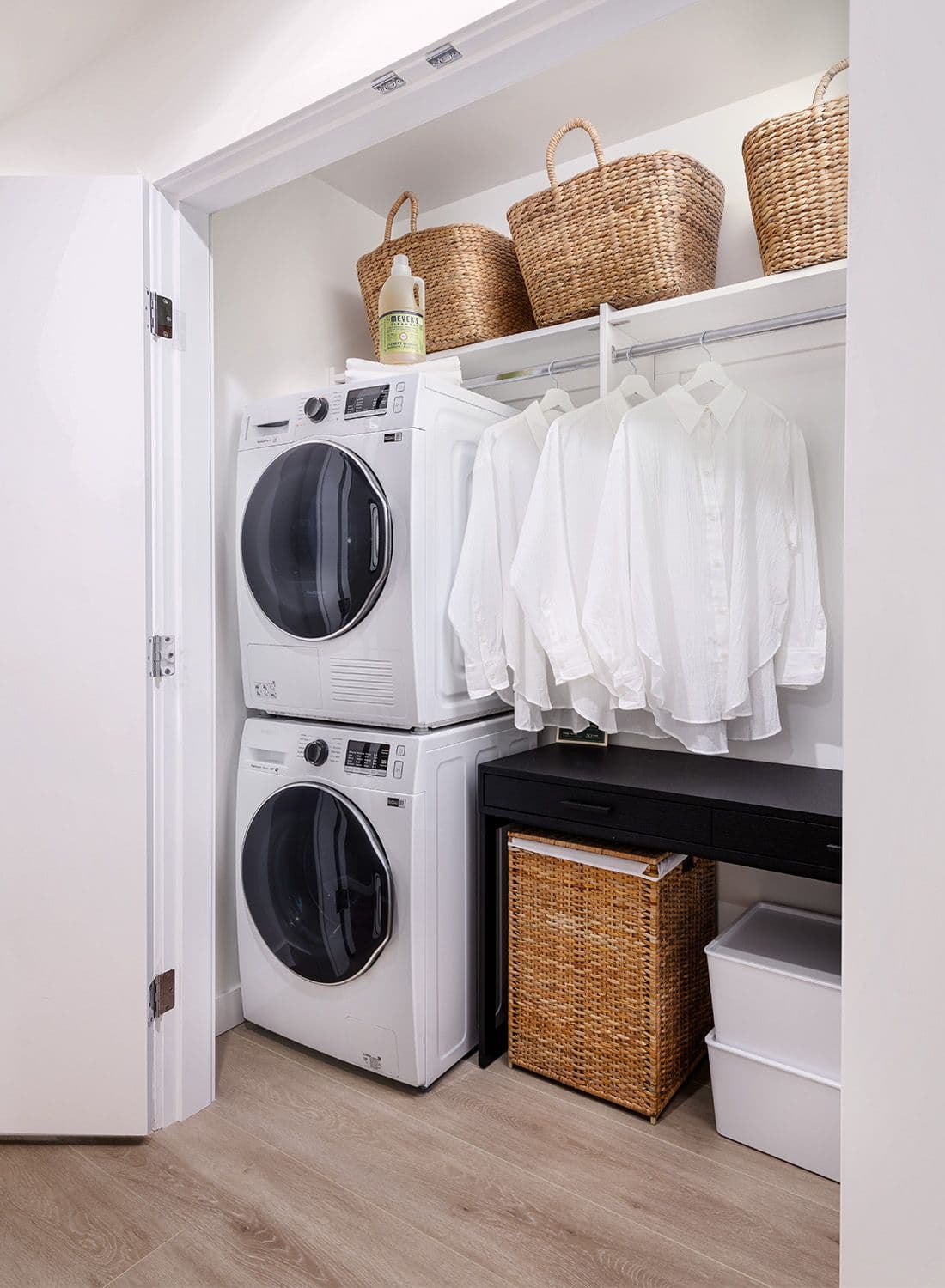 Century City Holland Park - Park Tower 1 – Laundry closet with a stacked white front-load washer and dryer, hanging shirts, and woven storage baskets on an upper shelf.