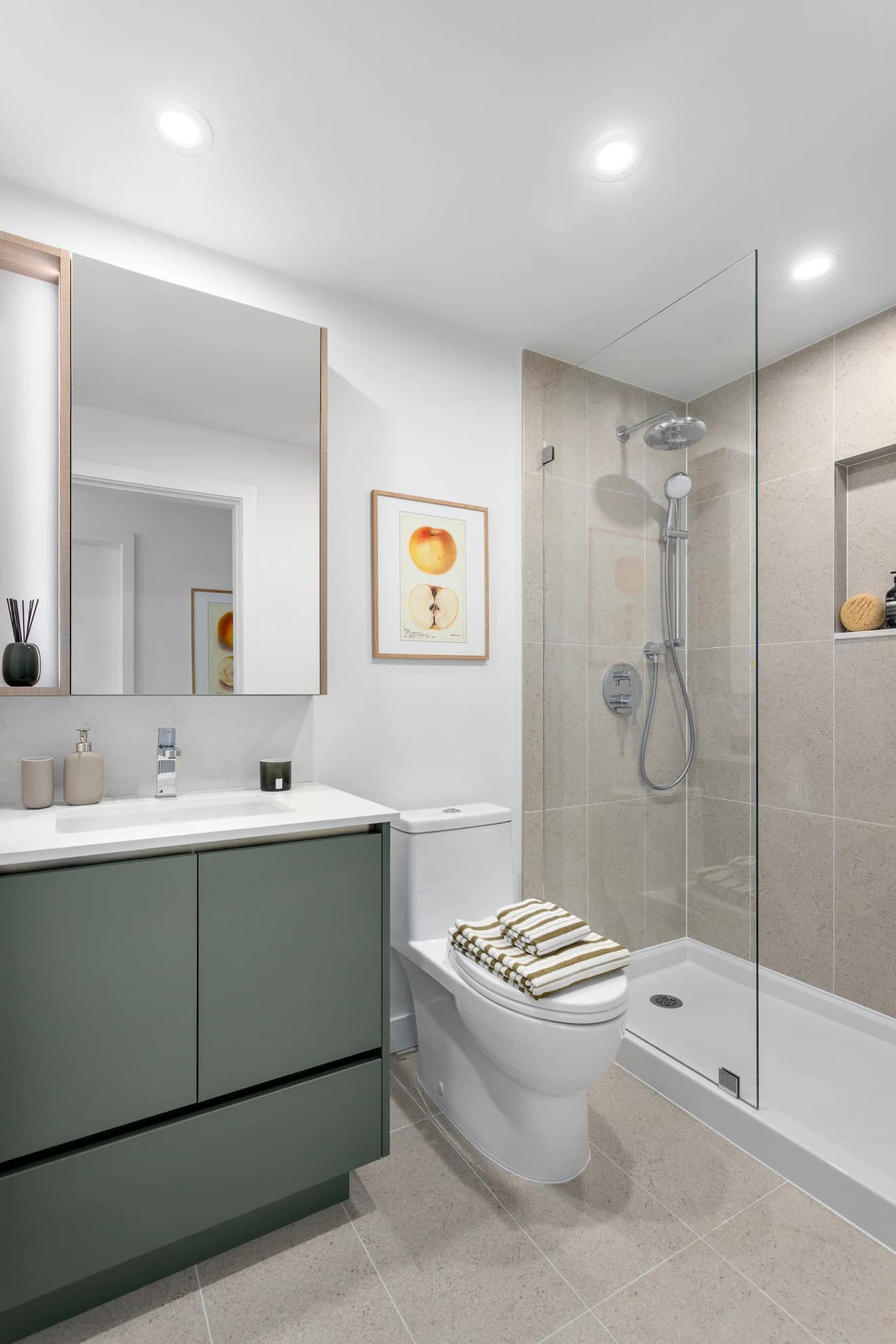 Century City Holland Park - Park Tower 1 – Bathroom with a glass-walled walk-in shower, green vanity with white countertop, and framed botanical art.