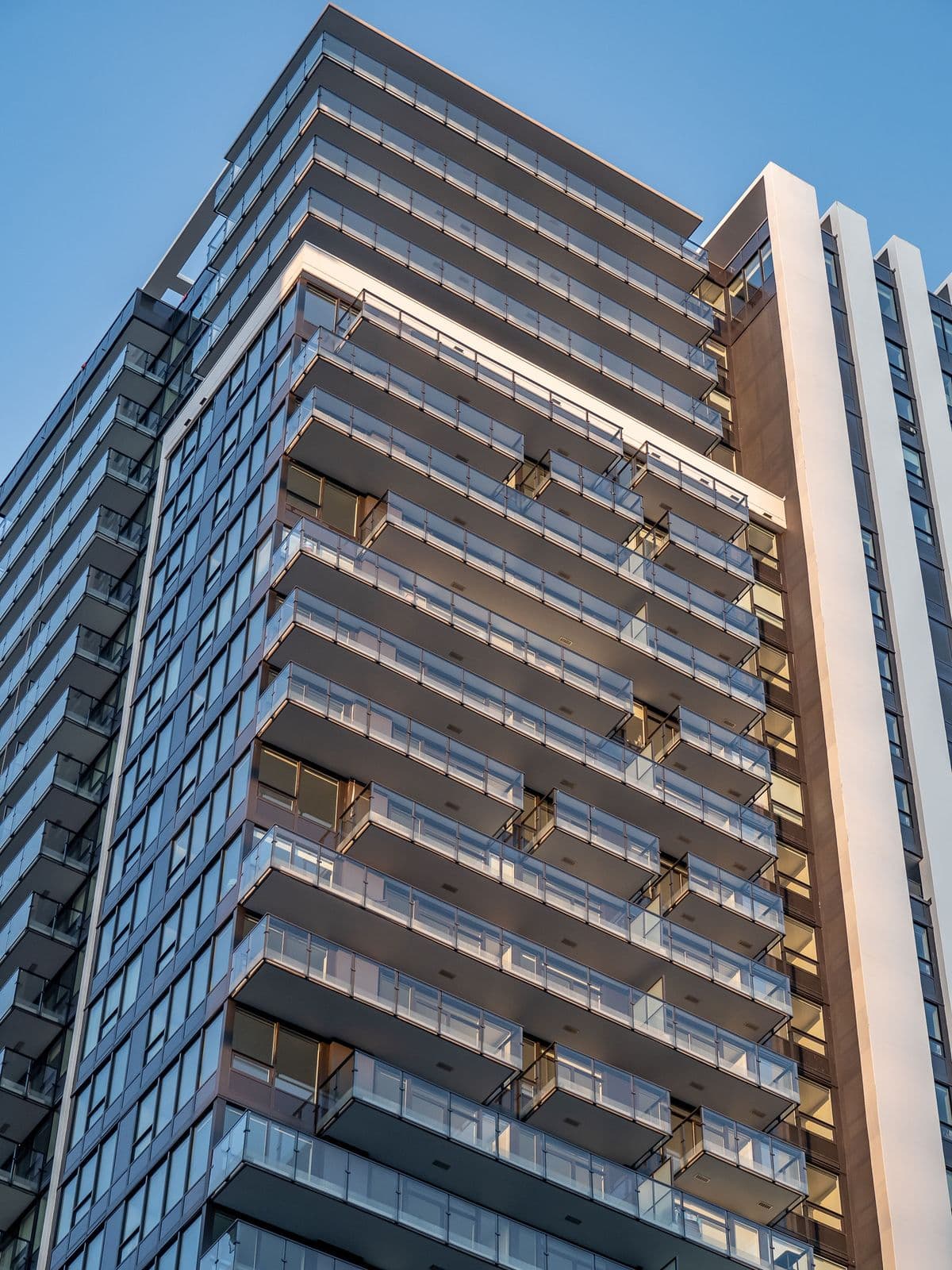 Ovation – Close-up upward view of the tower's glass balconies and facade catching warm sunlight against a clear blue sky.