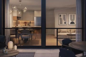 Azure Grove – Evening view from a balcony looking into a home's kitchen, dining table, and living room through glass sliding doors, with balcony furniture in the foreground.