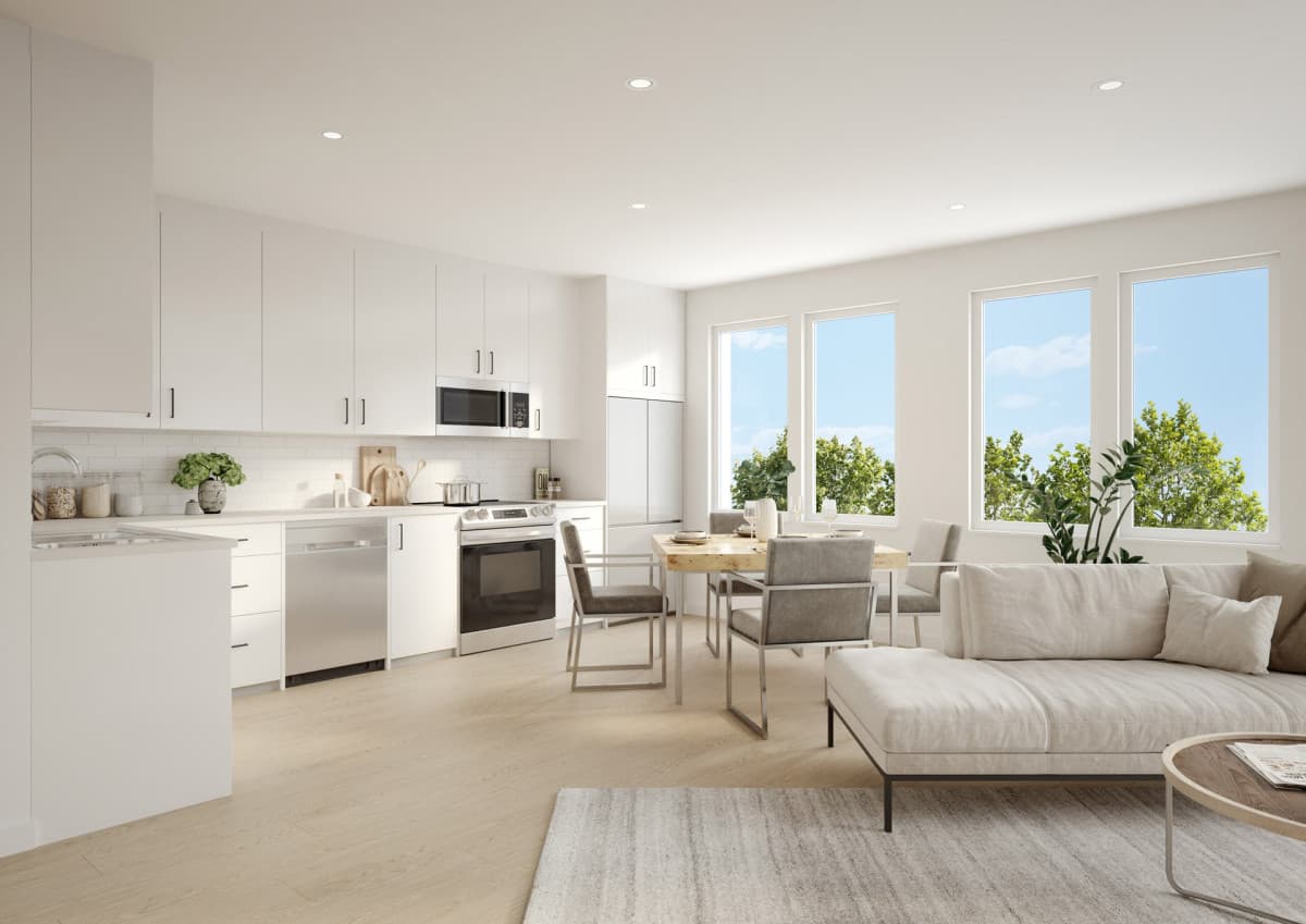 Montvue – Open-concept white kitchen with stainless appliances next to a dining table and living room seating, with large windows showing trees.
